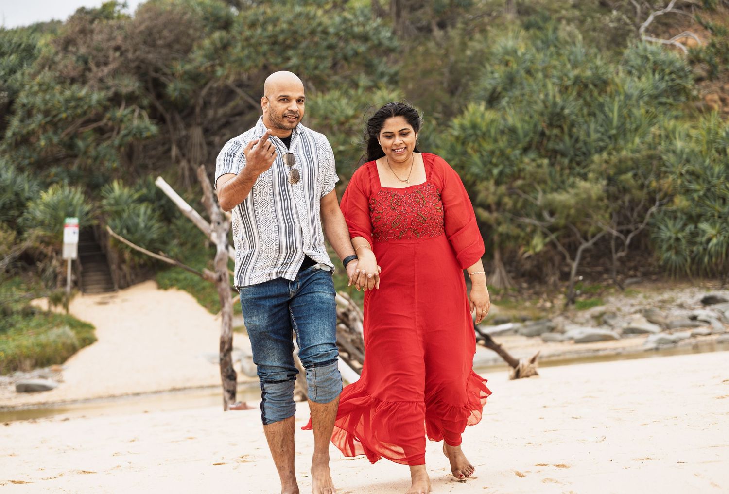 Playful beach photoshoot with couple walking along shoreline.