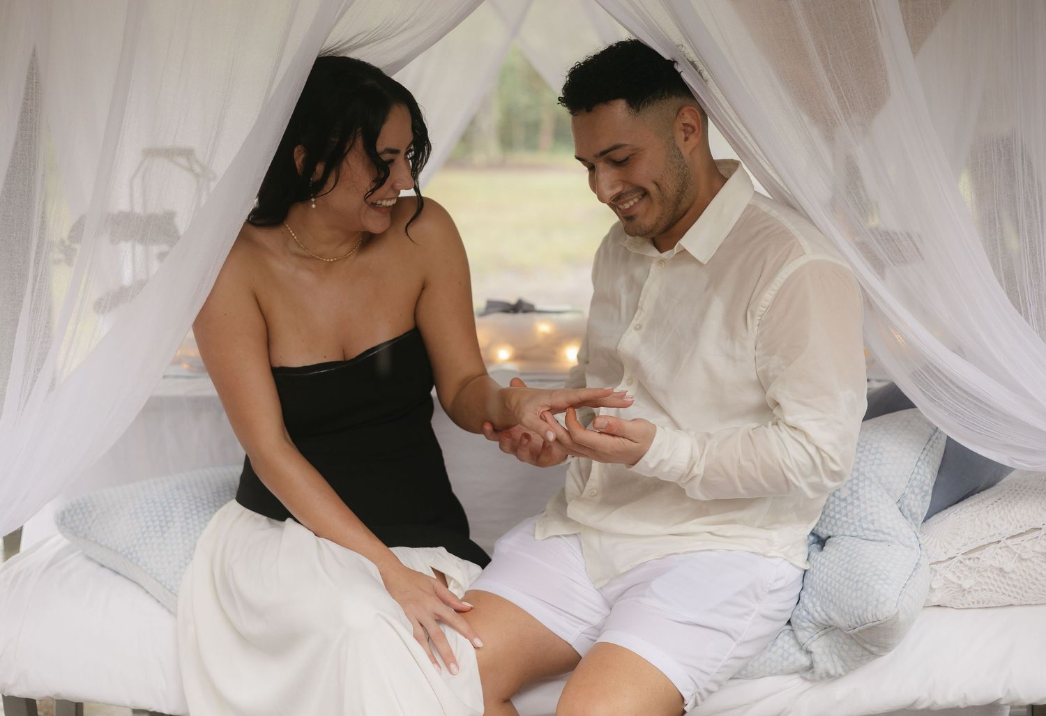 Romantic couple embracing under white canopy with natural lighting.