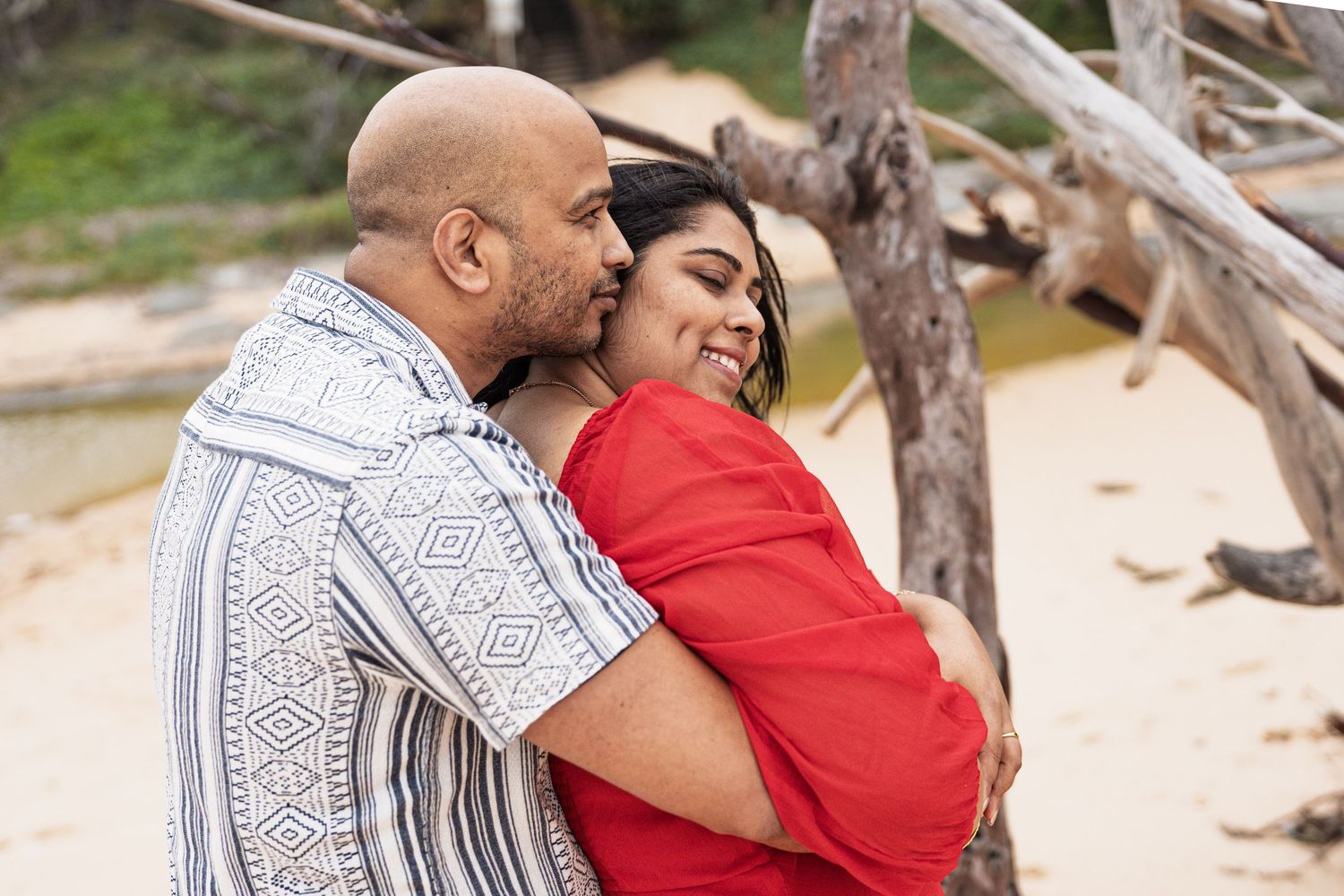 Intimate embrace captured on a beach with natural driftwood elements.