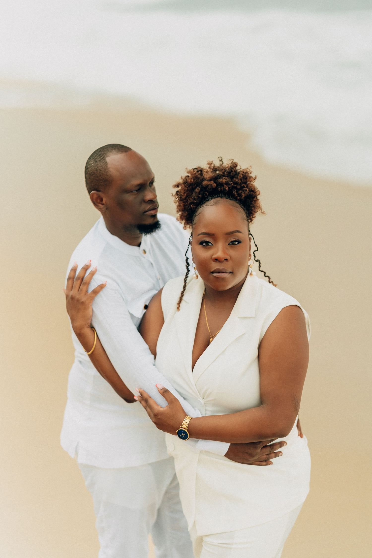 A playful beach photoshoot featuring a couple in white outfits against a sandy backdrop.
