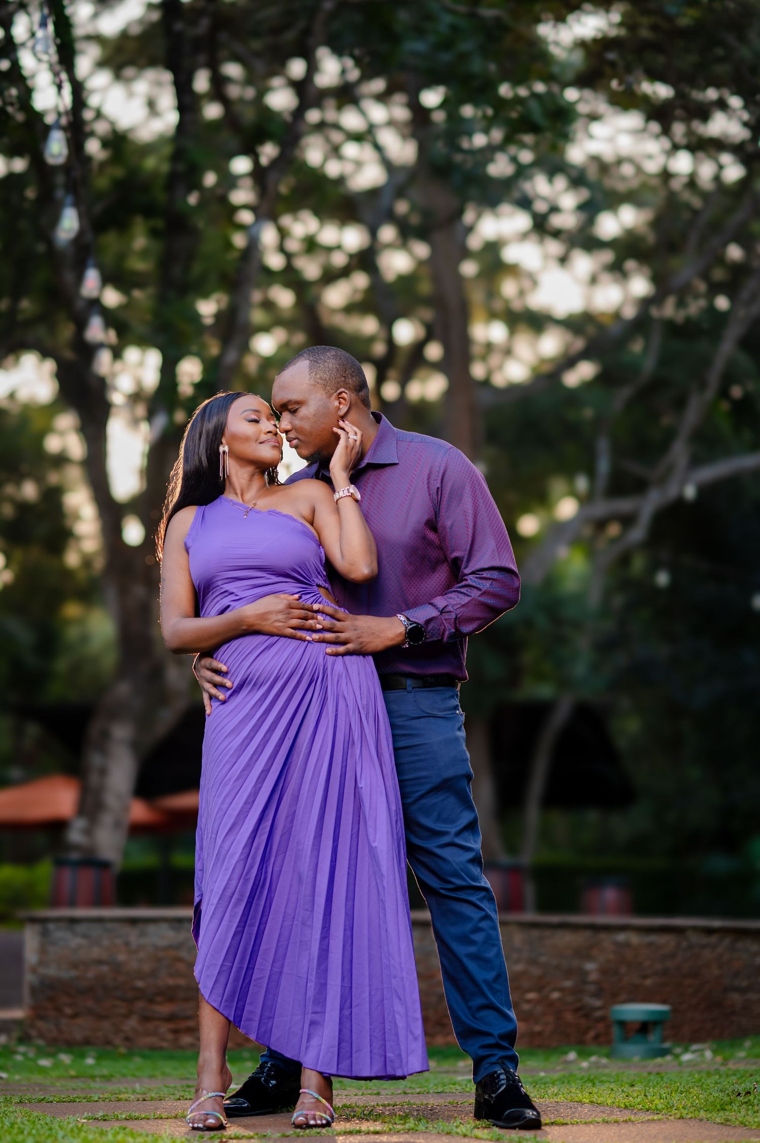 Romantic couple in coordinating purple outfits embrace in an outdoor garden setting at sunset.