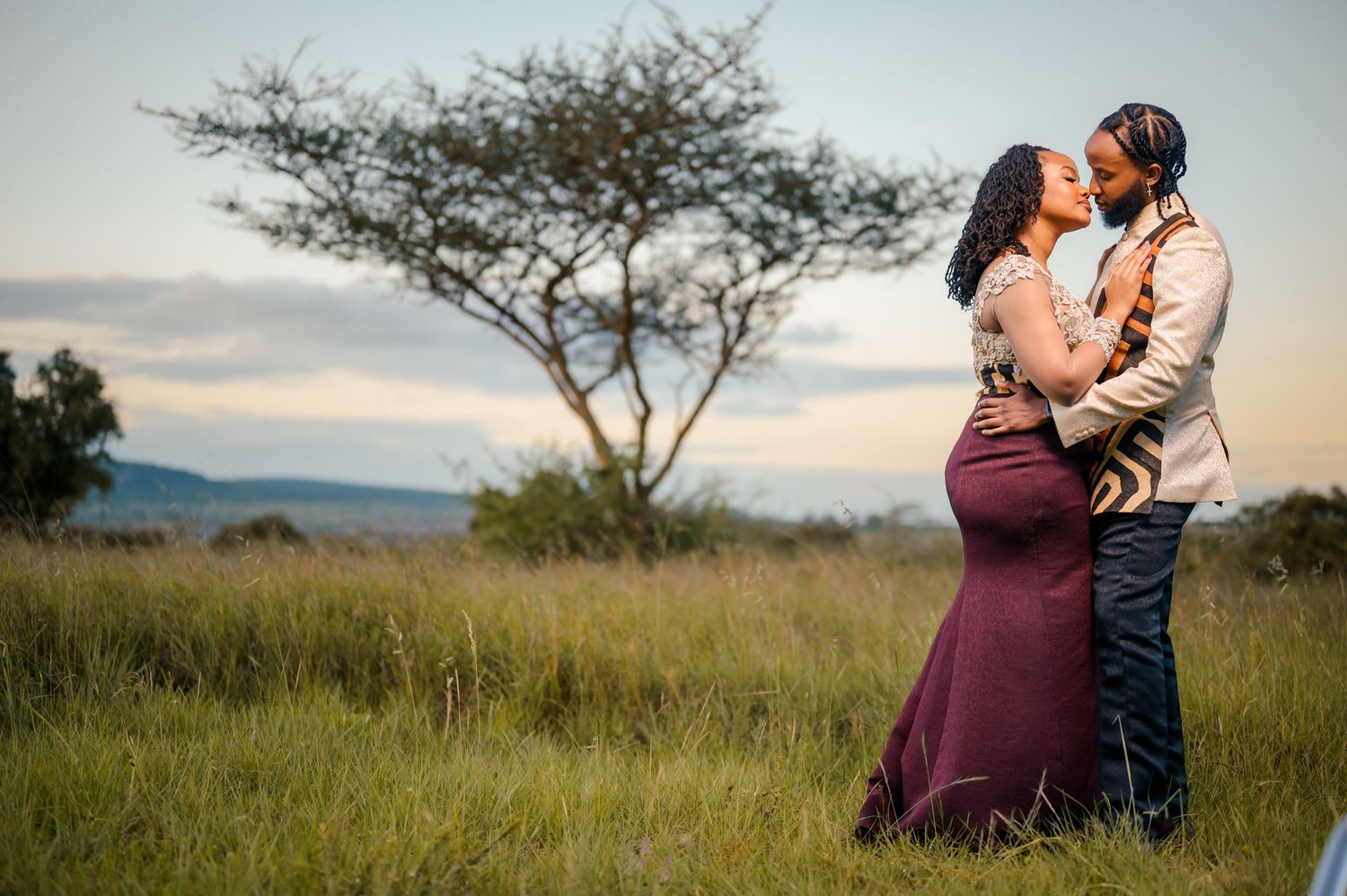 Loving couple sharing intimate moment in African savanna landscape at dusk.