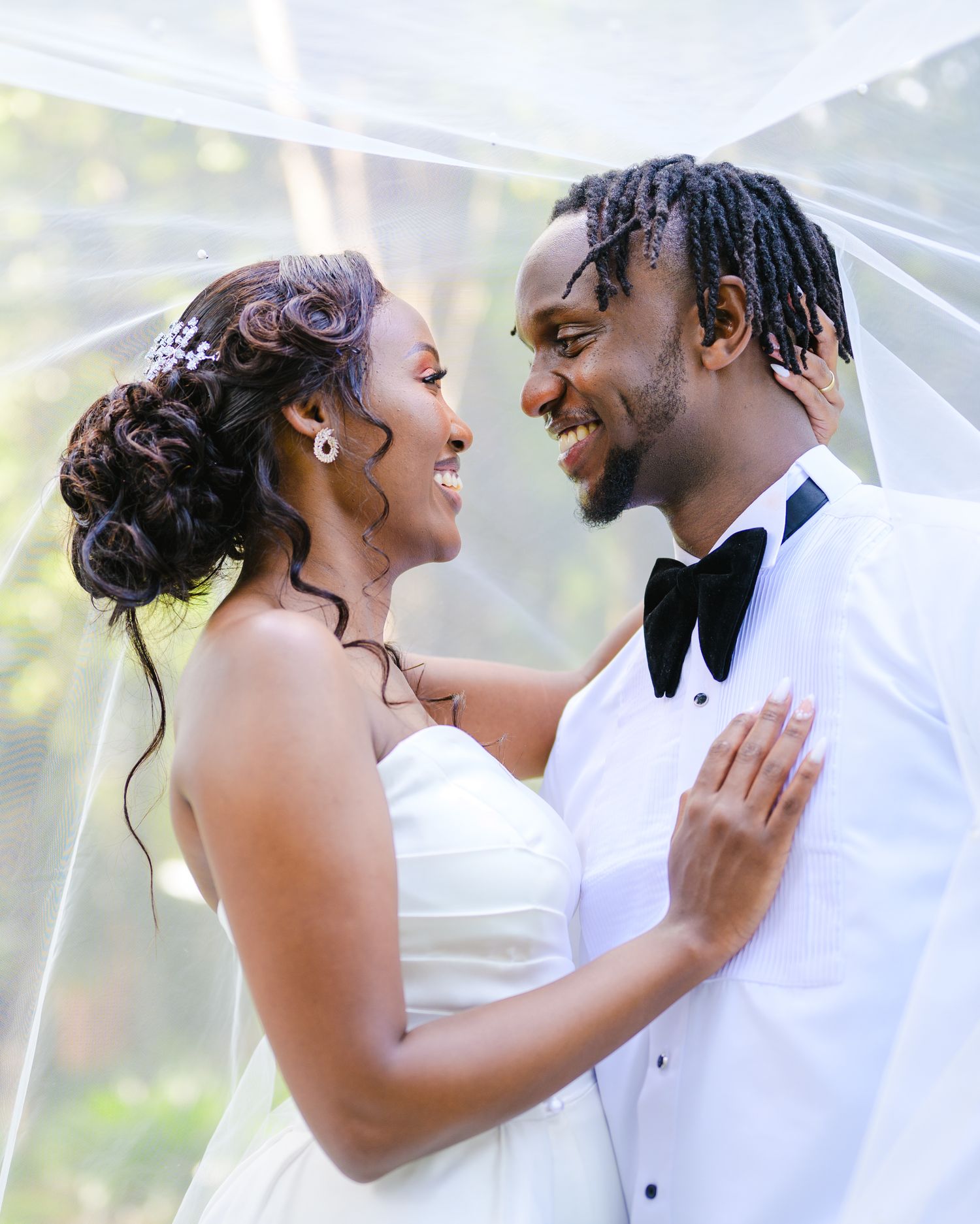 Joyful wedding couple sharing loving moment under sheer veil outdoors.
