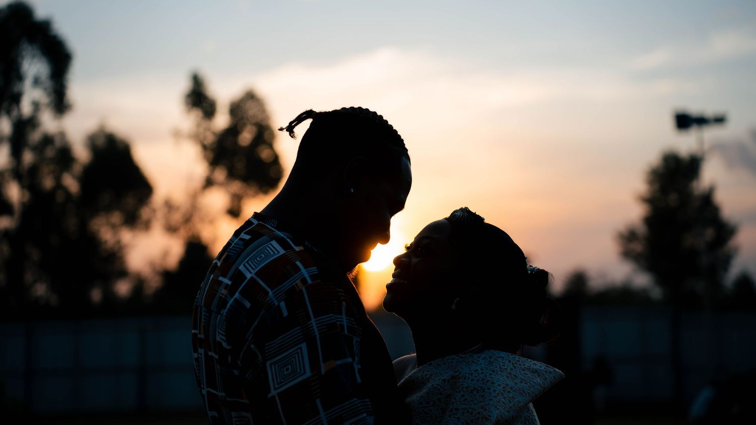 Silhouetted figures against dramatic sunset sky with trees in background.