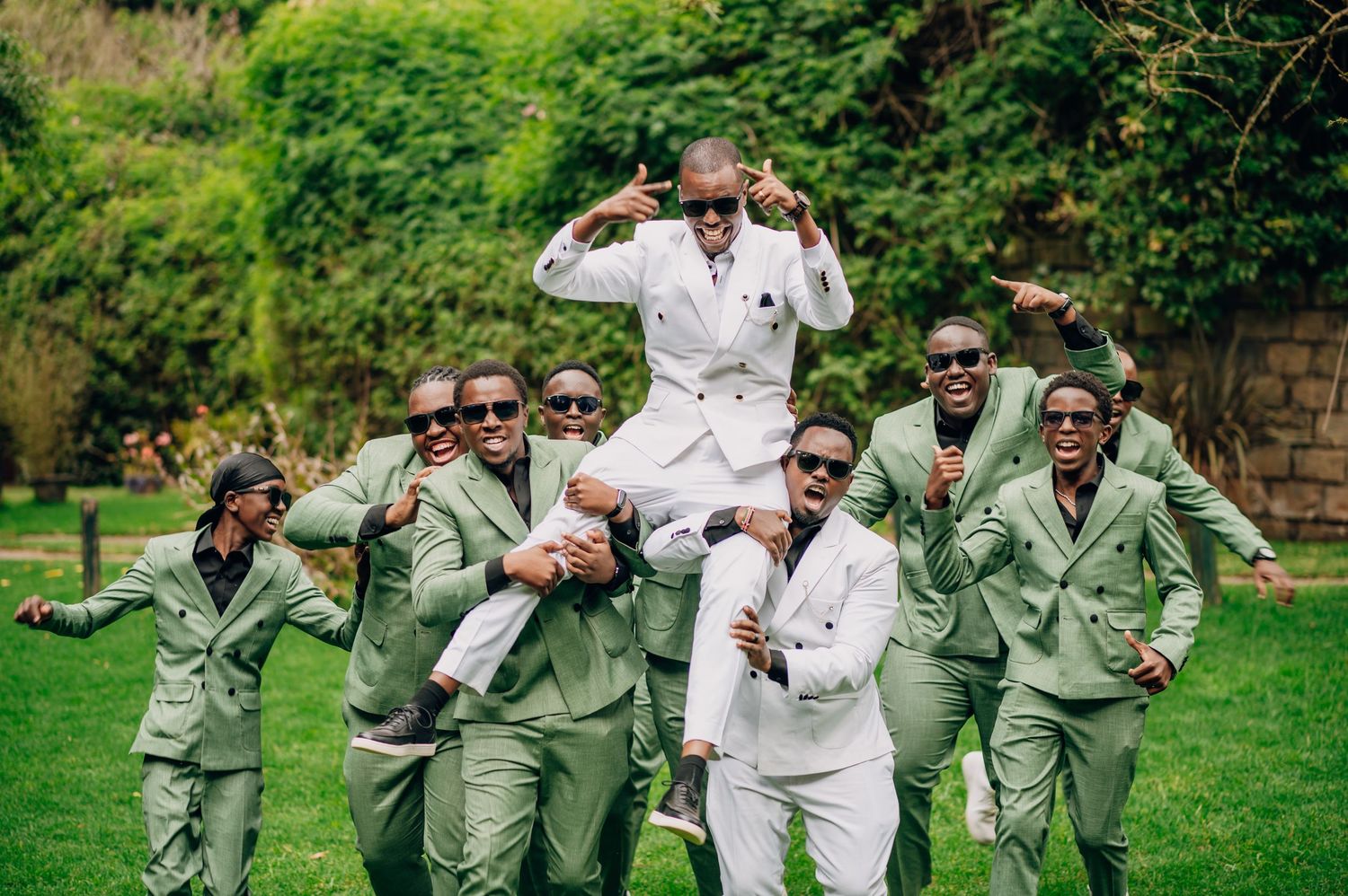 A joyful group photo with people wearing matching sage green outfits in a garden setting.