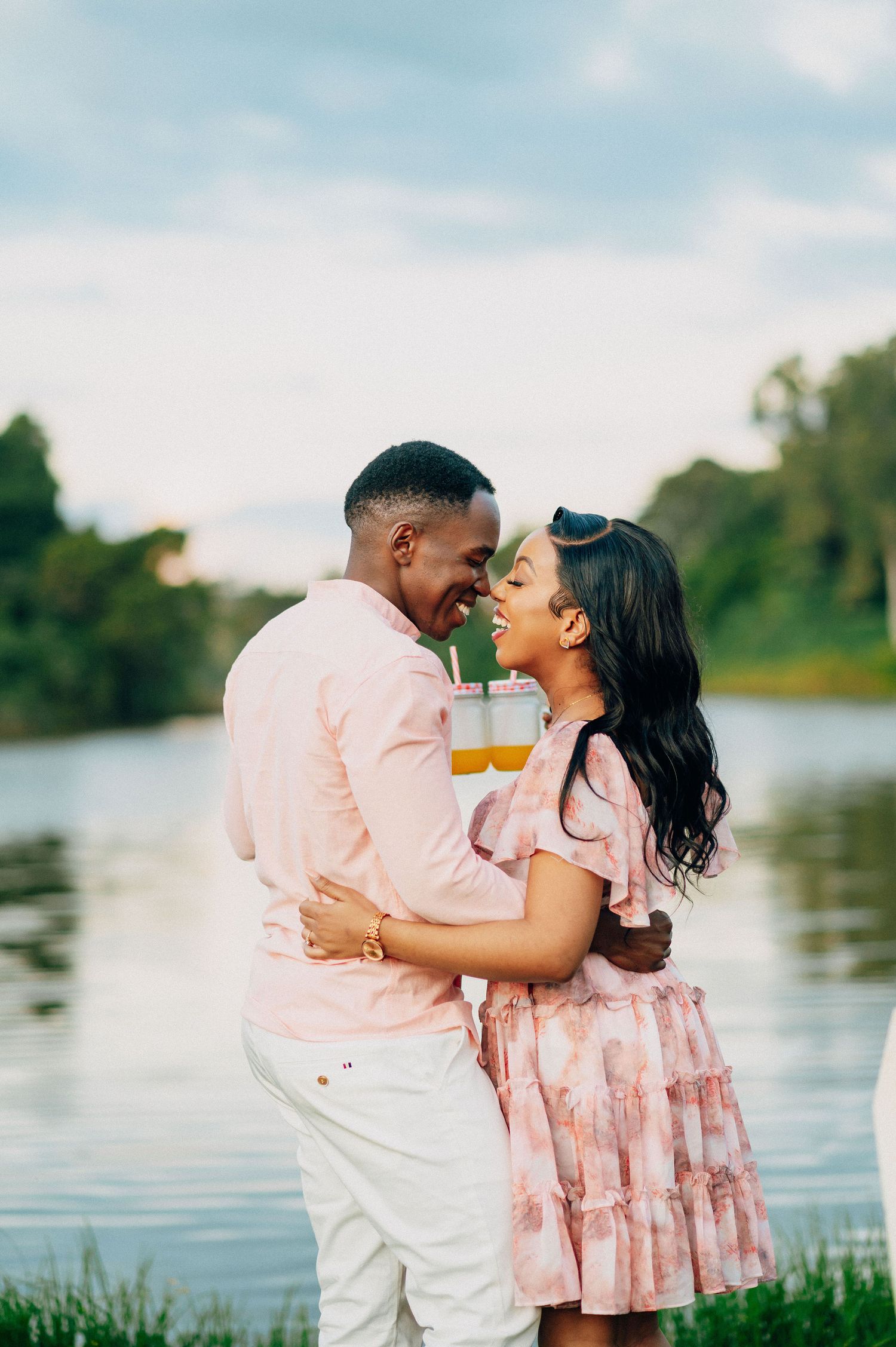 A romantic lakeside photoshoot with a couple wearing coordinated pink and white outfits.