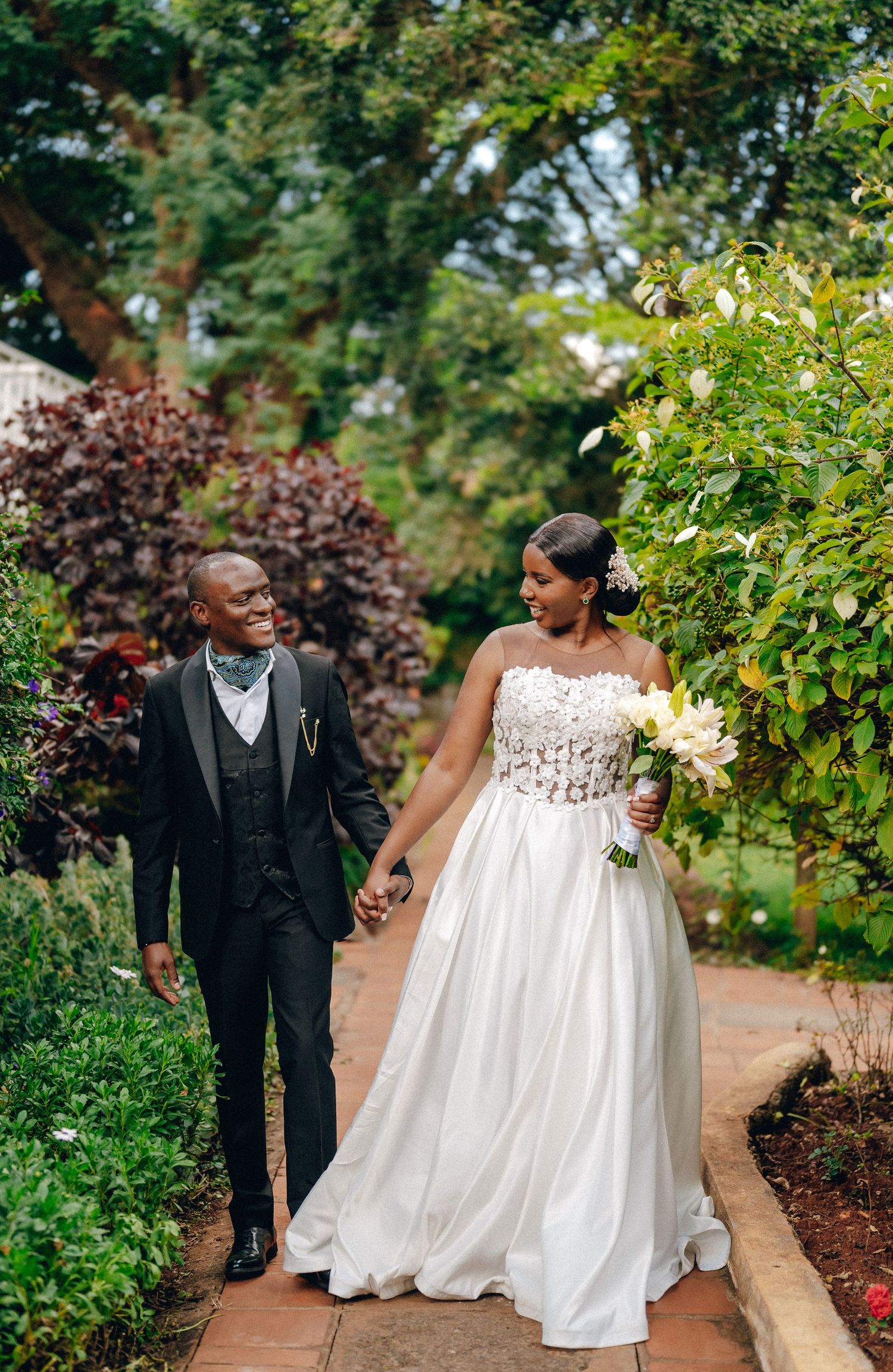 Couple walking and laughing together in a lush garden setting during their wedding celebration.