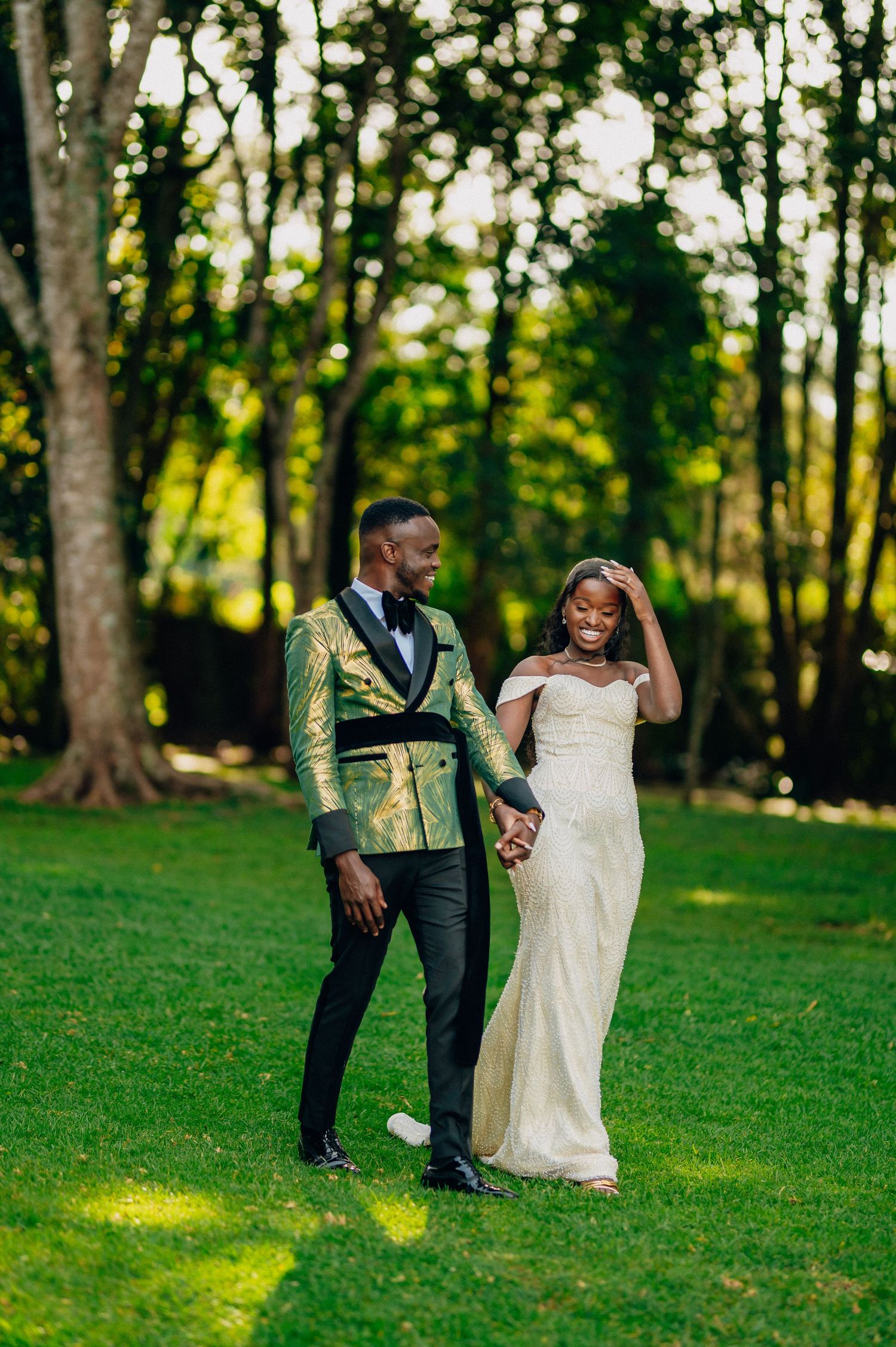 Newlyweds in elegant white and green attire share romantic moment on grassy lawn.