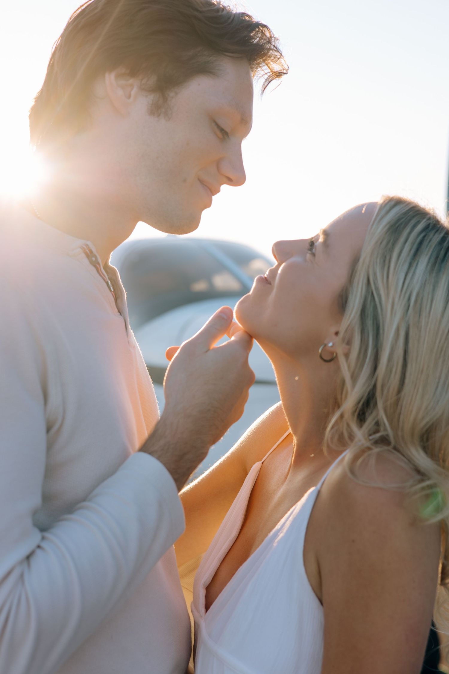 Romantic couple nearly kissing in golden backlight with a small plane visible behind them outdoors.