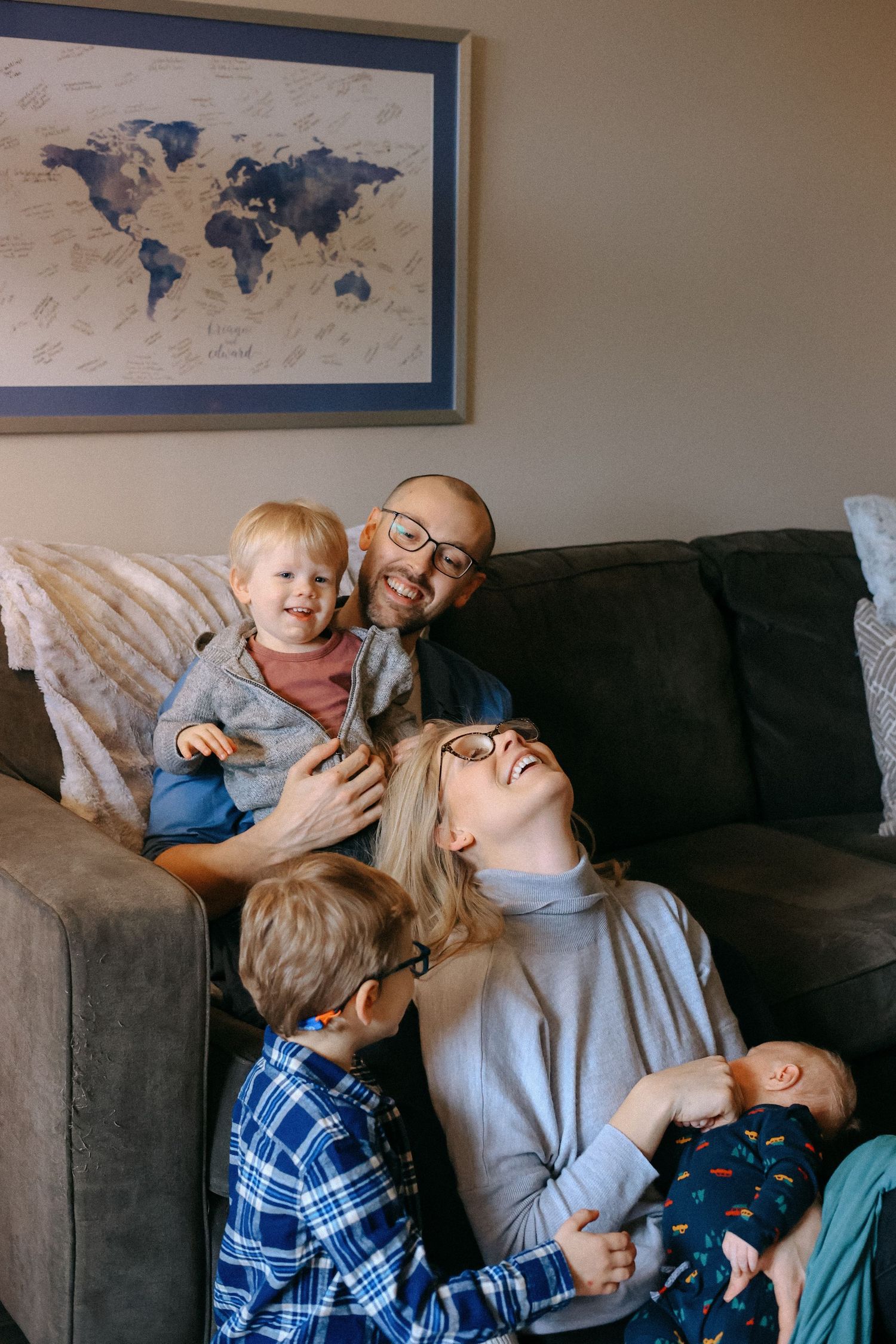 Happy family with three children laughing together on a gray couch beneath a world map.