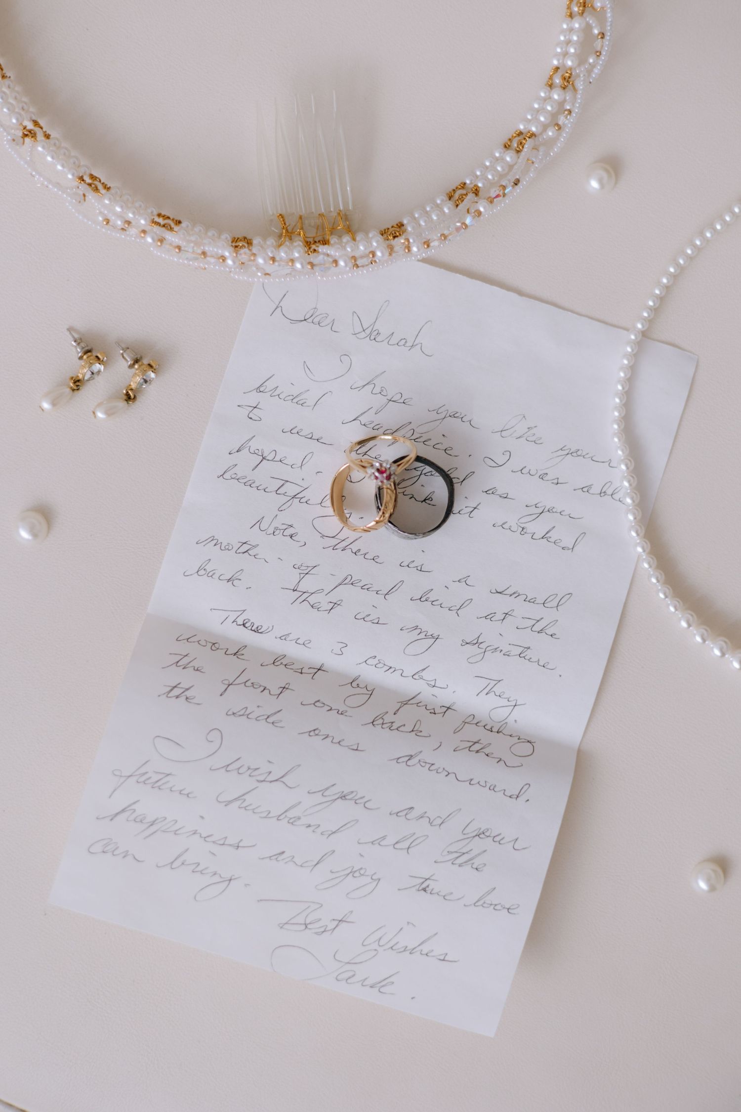 Wedding flat lay featuring handwritten letter, engagement rings, pearl hair comb, and gold earrings.