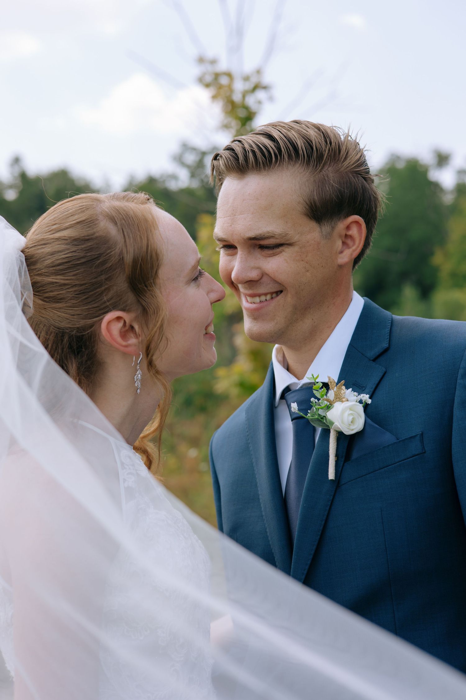 Smiling bride and groom share a joyful moment outdoors with veil flowing on their wedding day.