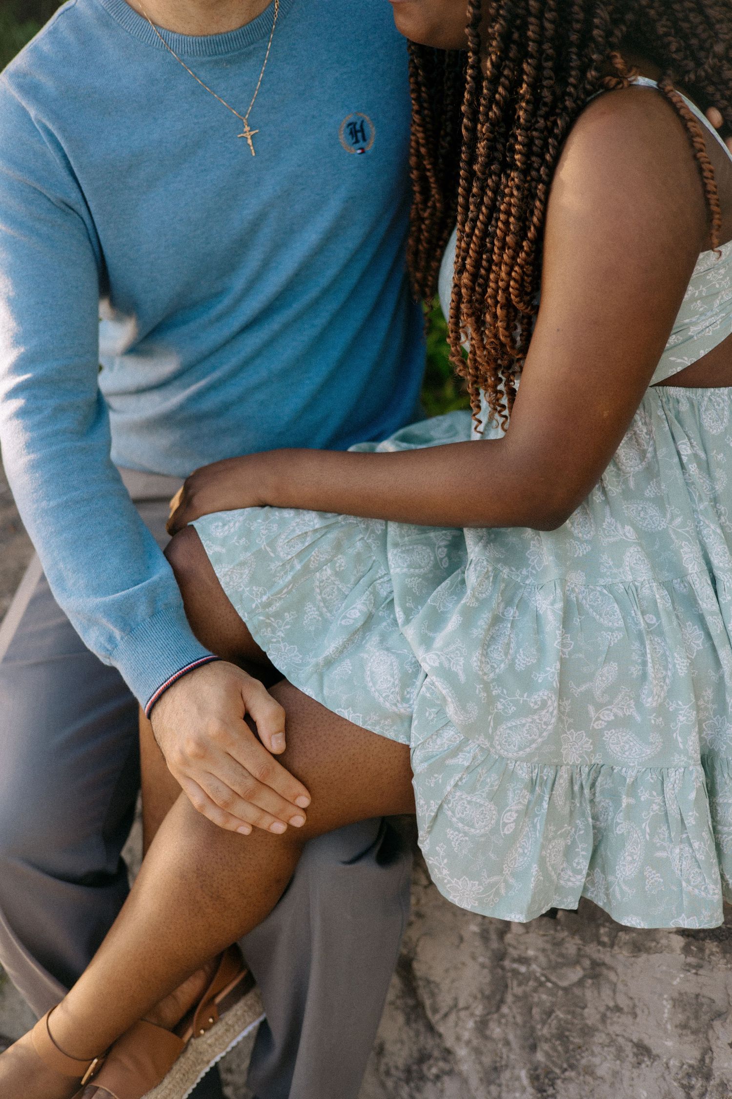 Close-up of an interracial couple holding hands, woman in mint dress, man in blue sweater.