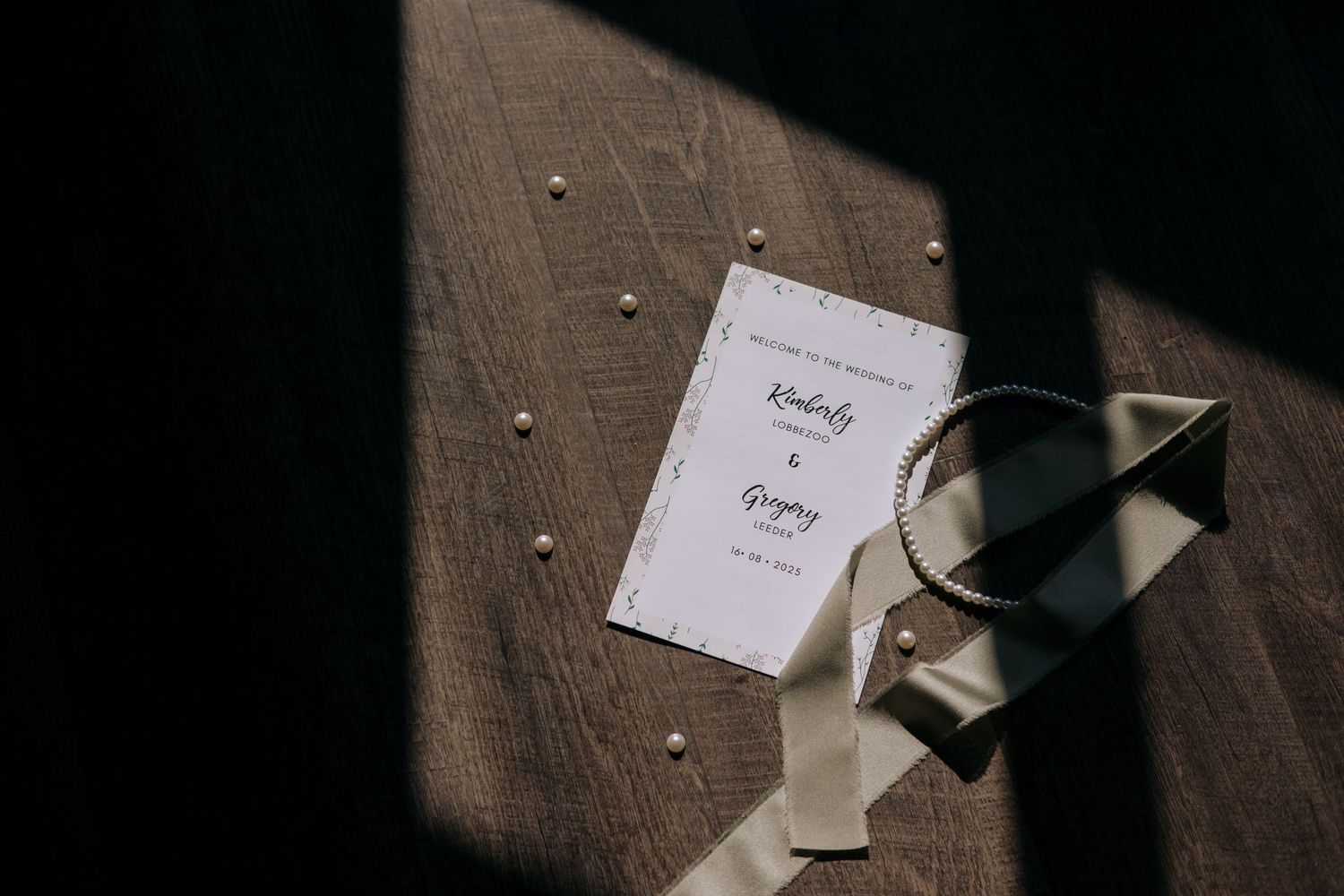 A wedding program displayed with pearl accents and ribbon on a dark surface.
