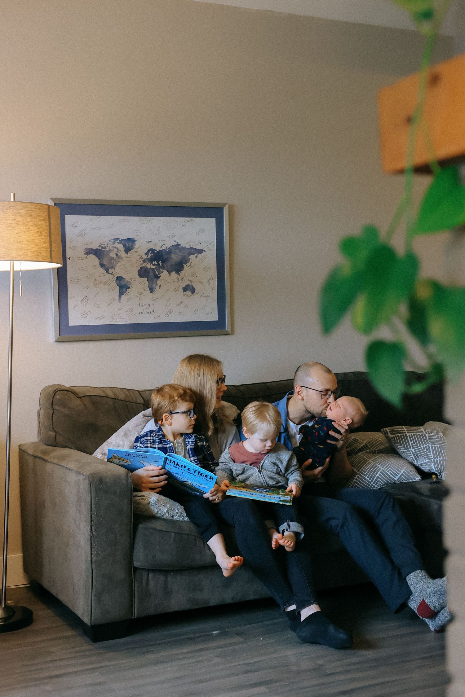 Family of five sitting together on a couch reading books beneath a framed world map.