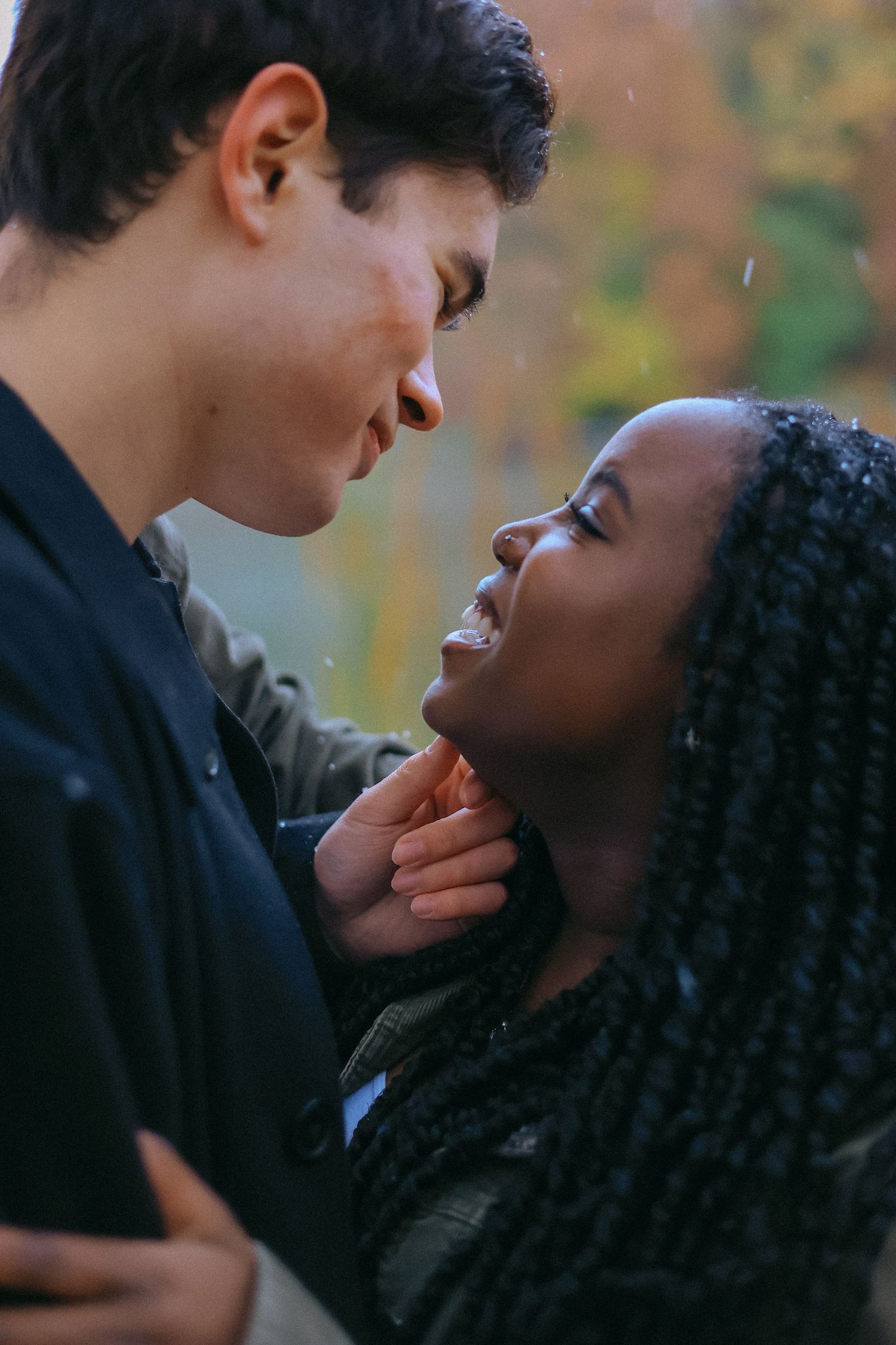 Interracial couple sharing a romantic almost-kiss moment outdoors in the rain with fall colors.