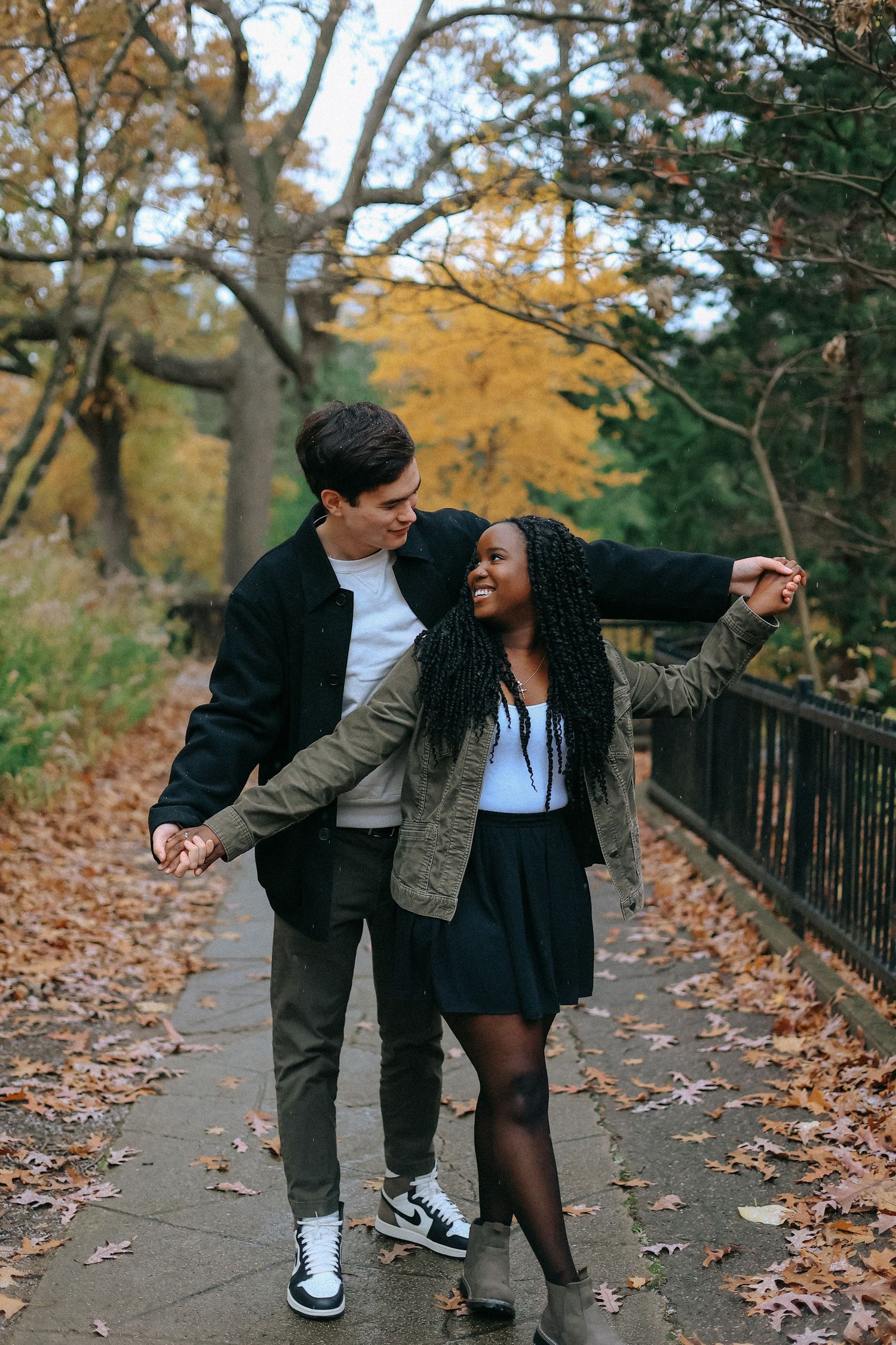 Happy interracial couple dancing on a leaf-covered path surrounded by golden autumn trees.