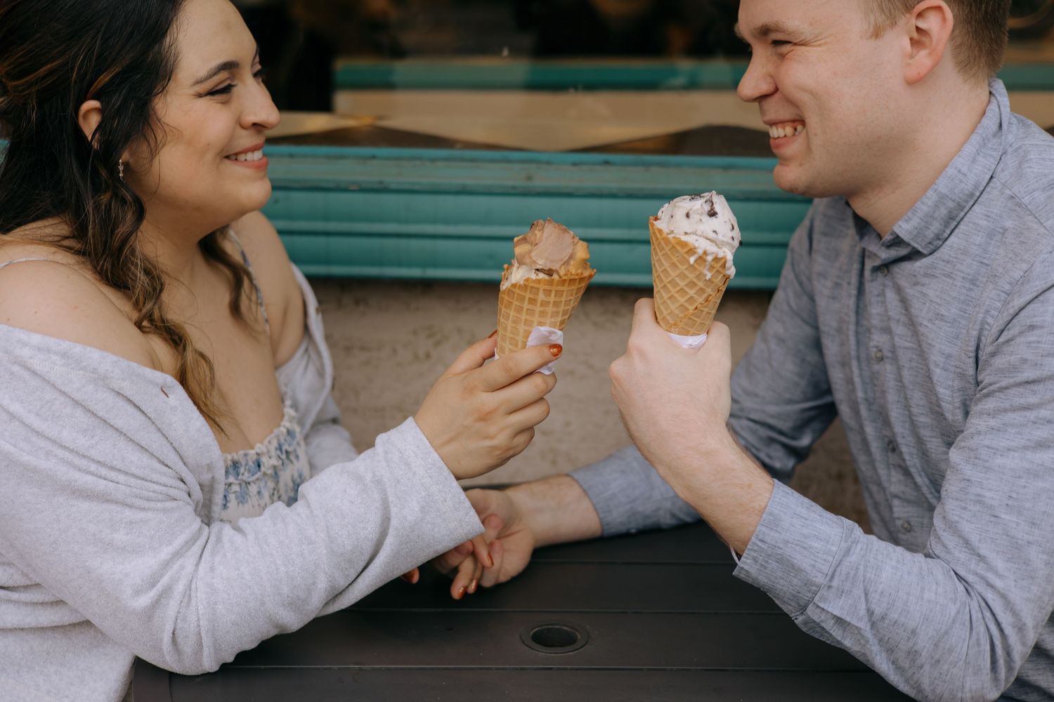 Happy couple sharing ice cream cones together while sitting at an outdoor table on a date.