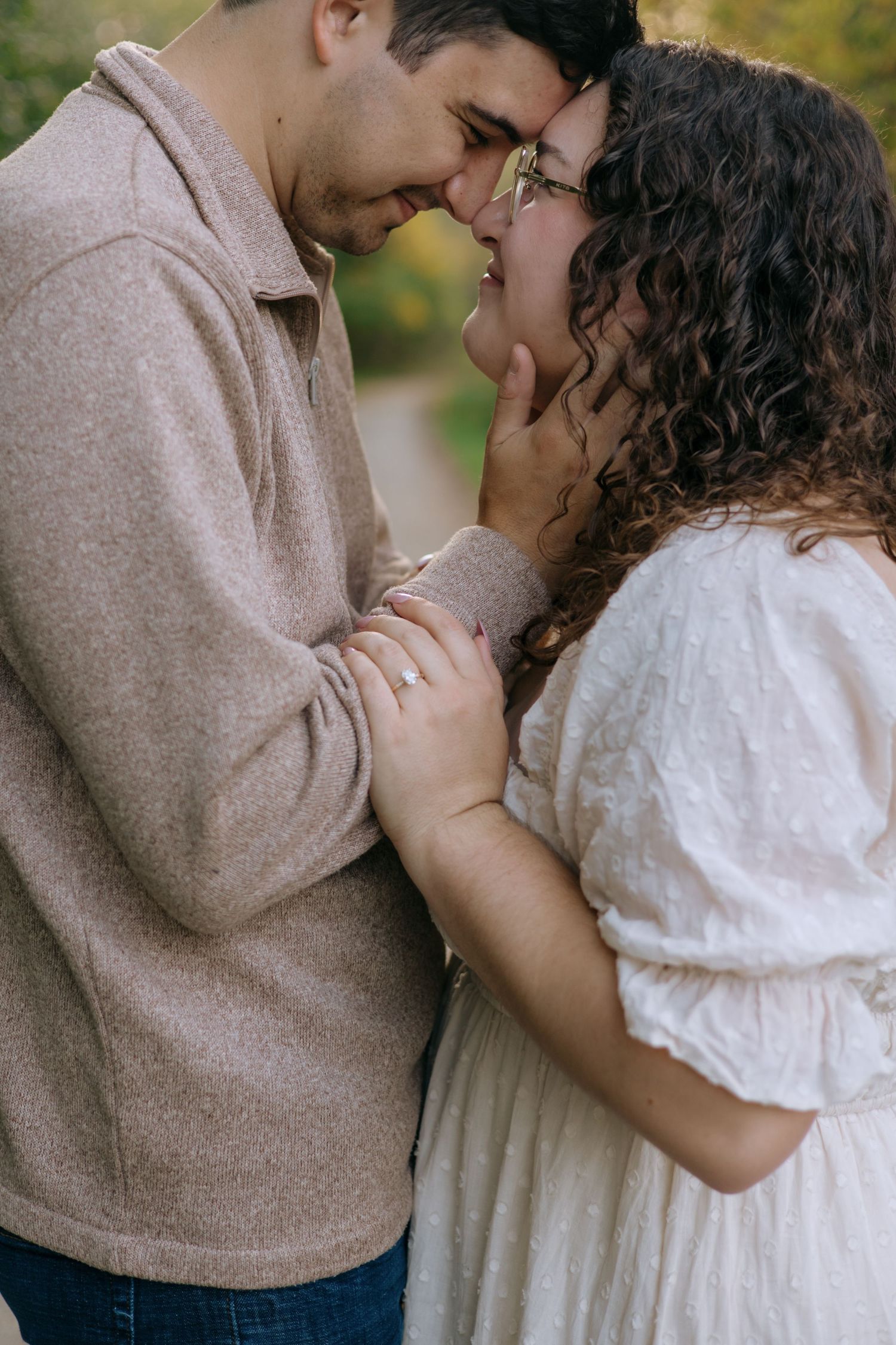 Couple sharing an intimate nose-to-nose moment outdoors in autumn, woman wearing white dress.