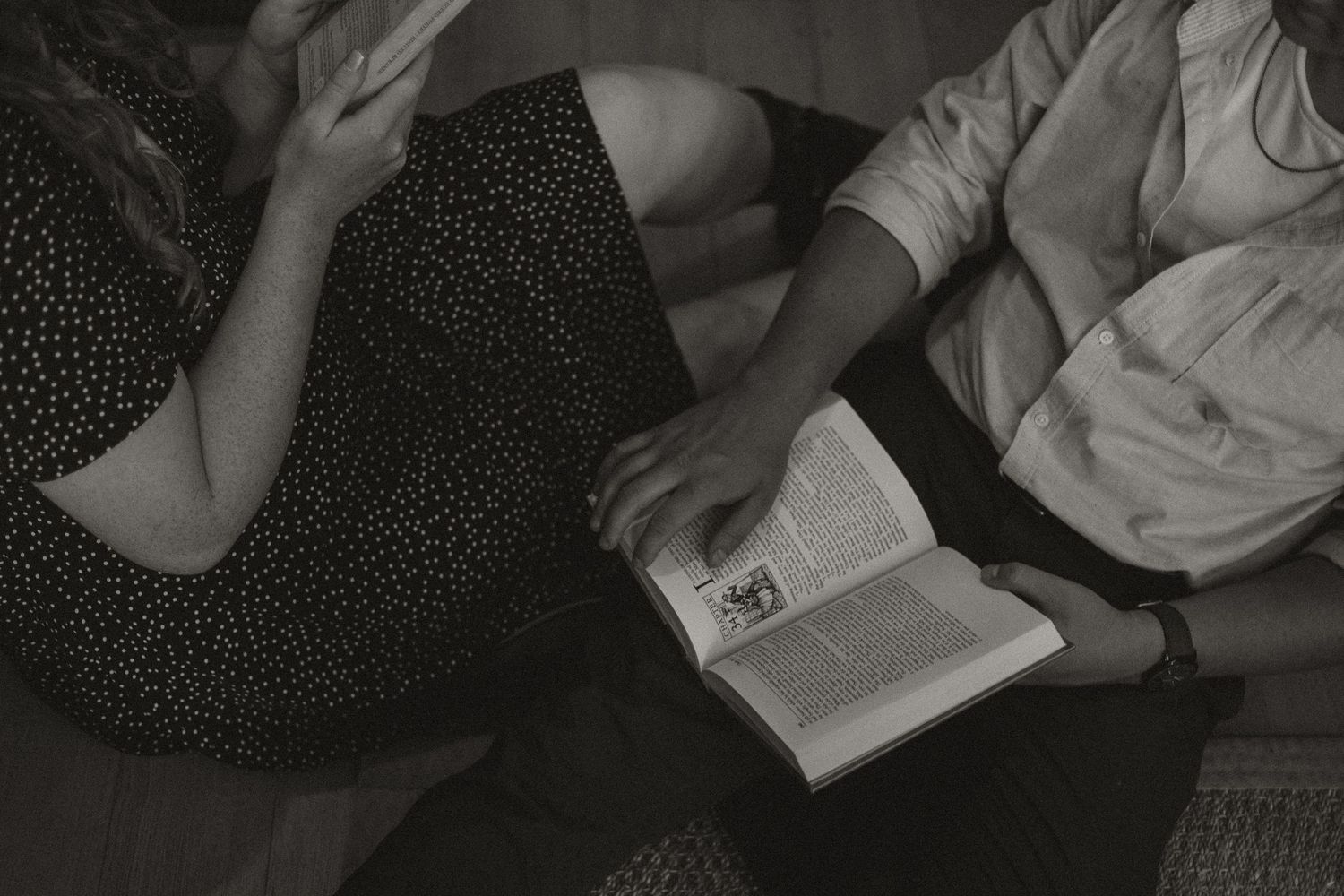 Black and white overhead view of two people sitting side by side sharing an open book indoors.