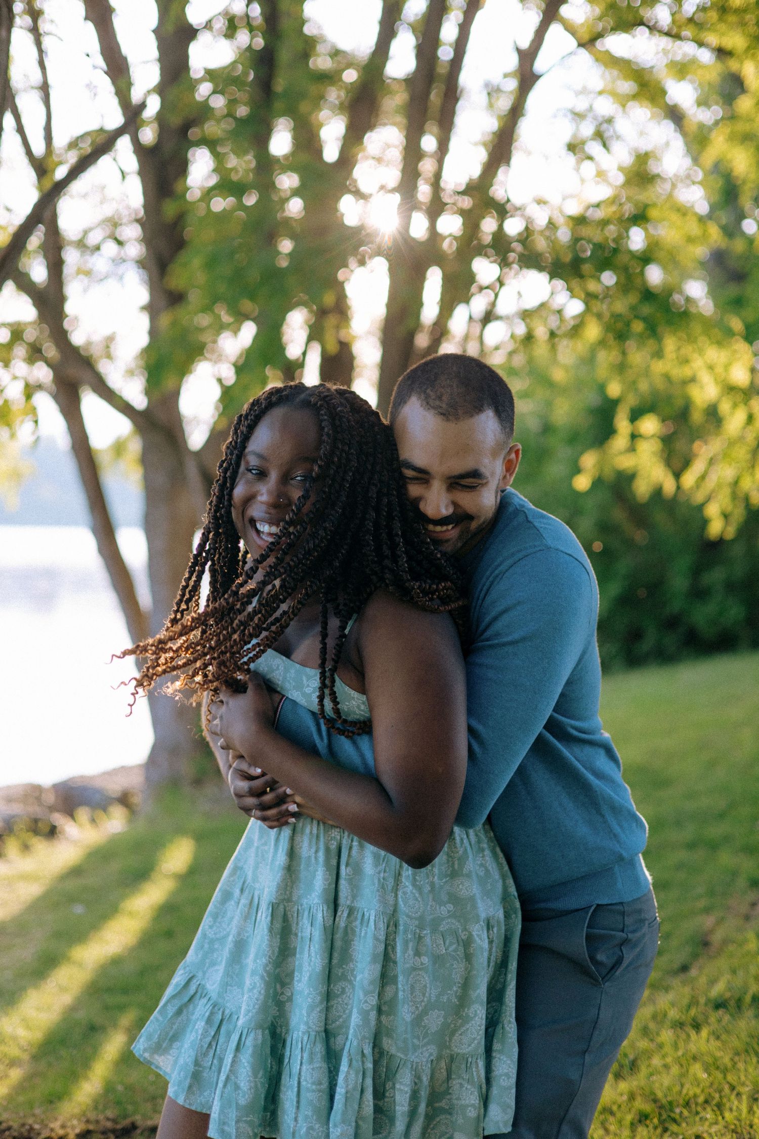 Joyful interracial couple hugging and laughing together in a sunny green park by a lake.