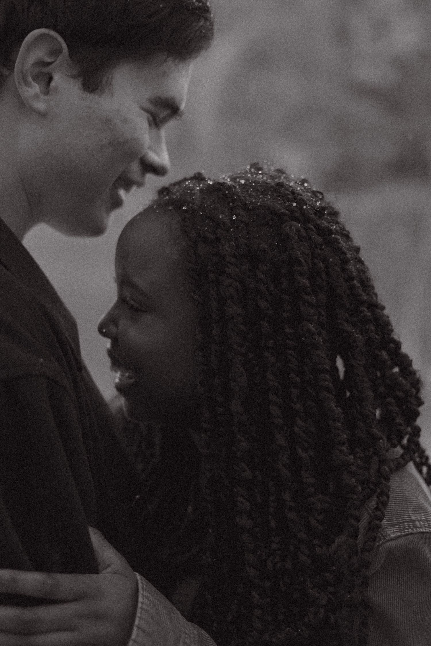 Black and white portrait of an interracial couple smiling and facing each other intimately.