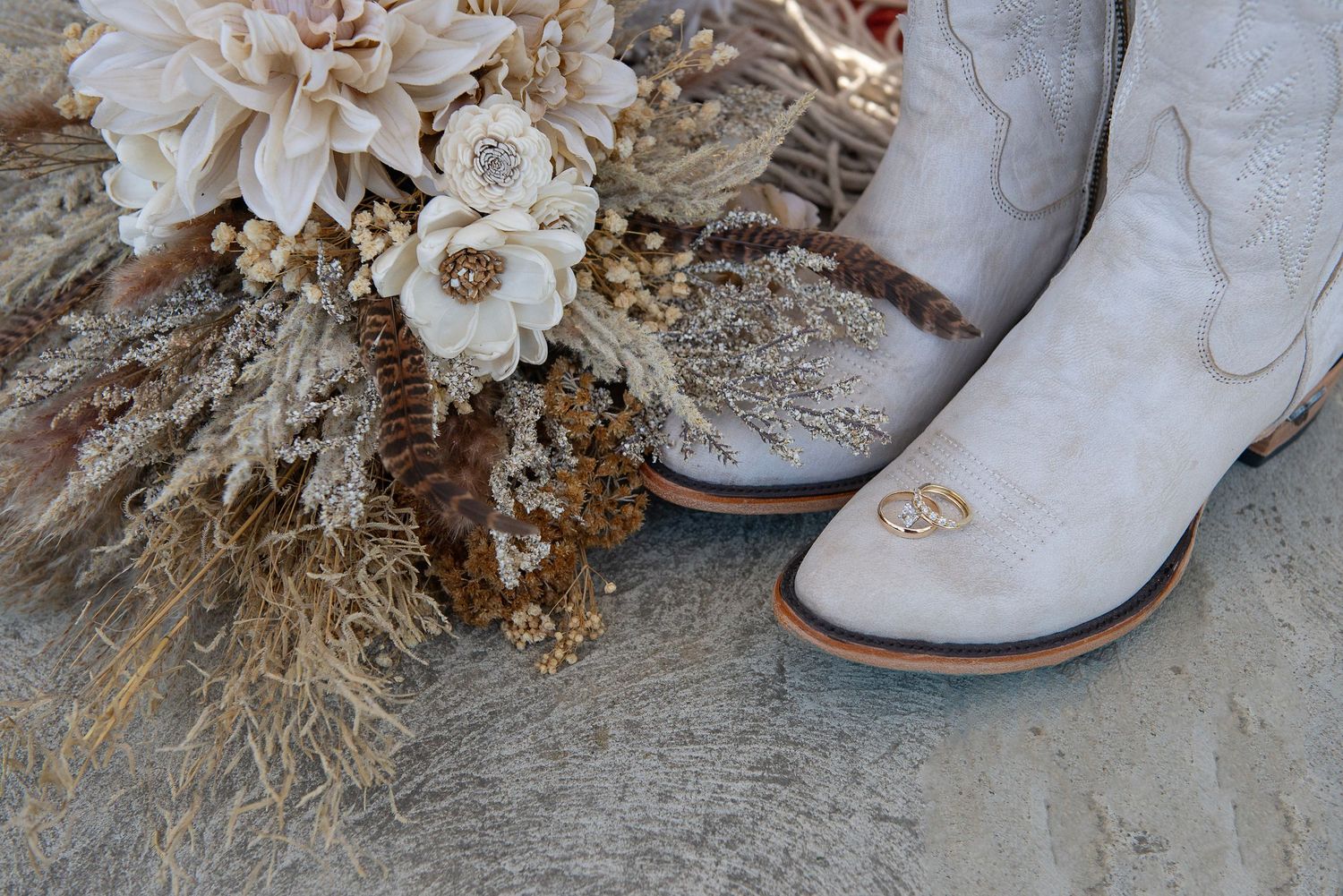 Vintage white boots next to dried floral arrangement on concrete surface.