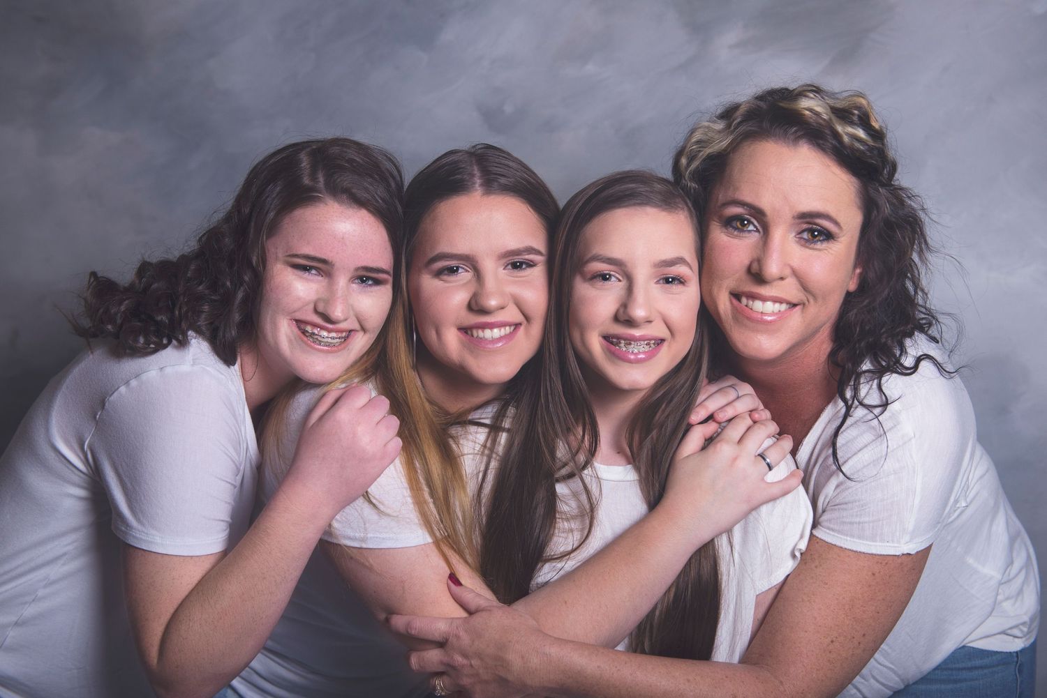 Studio portrait of friends in white tops against grey backdrop.