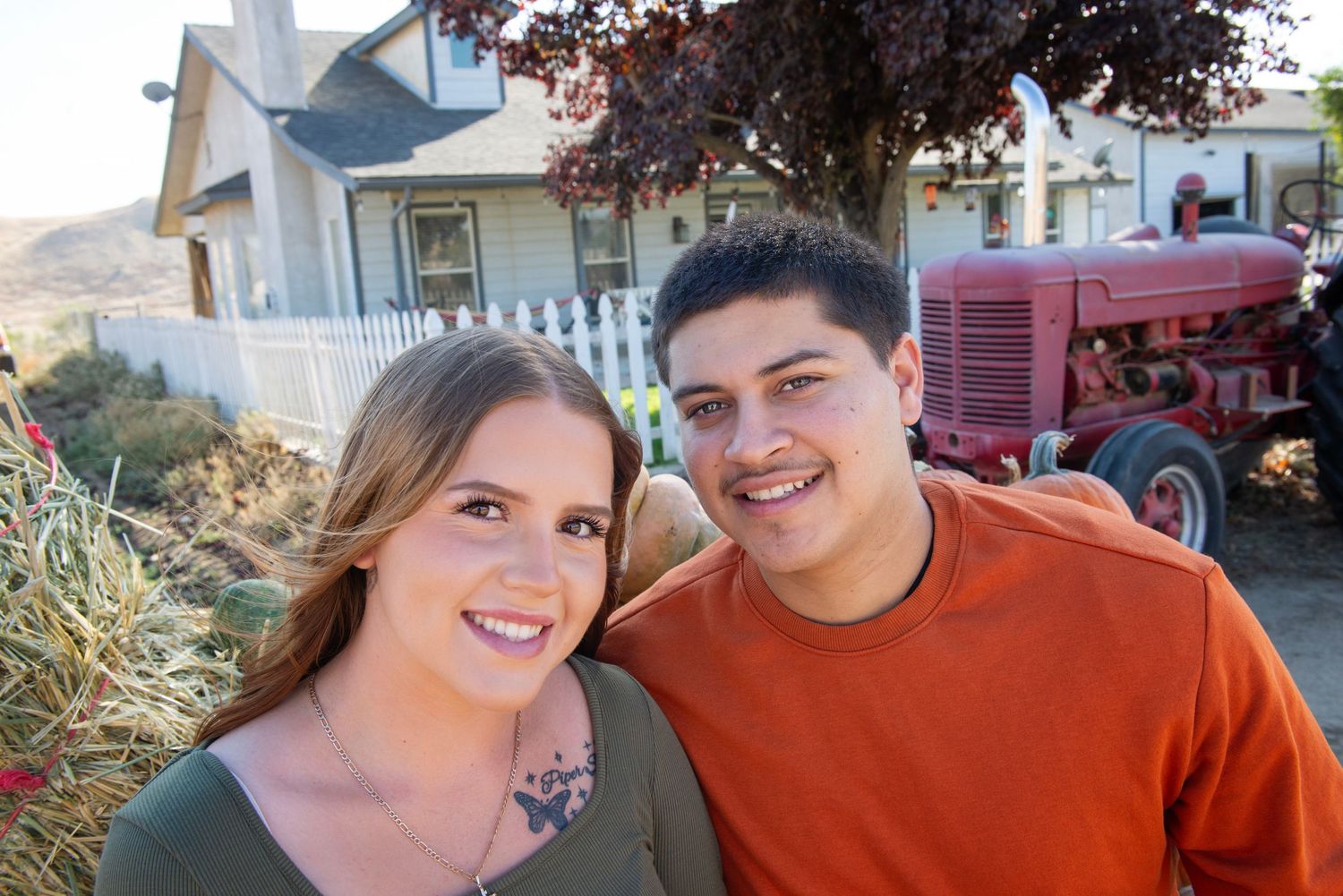 Casual couple poses outdoors with residential neighborhood in background.