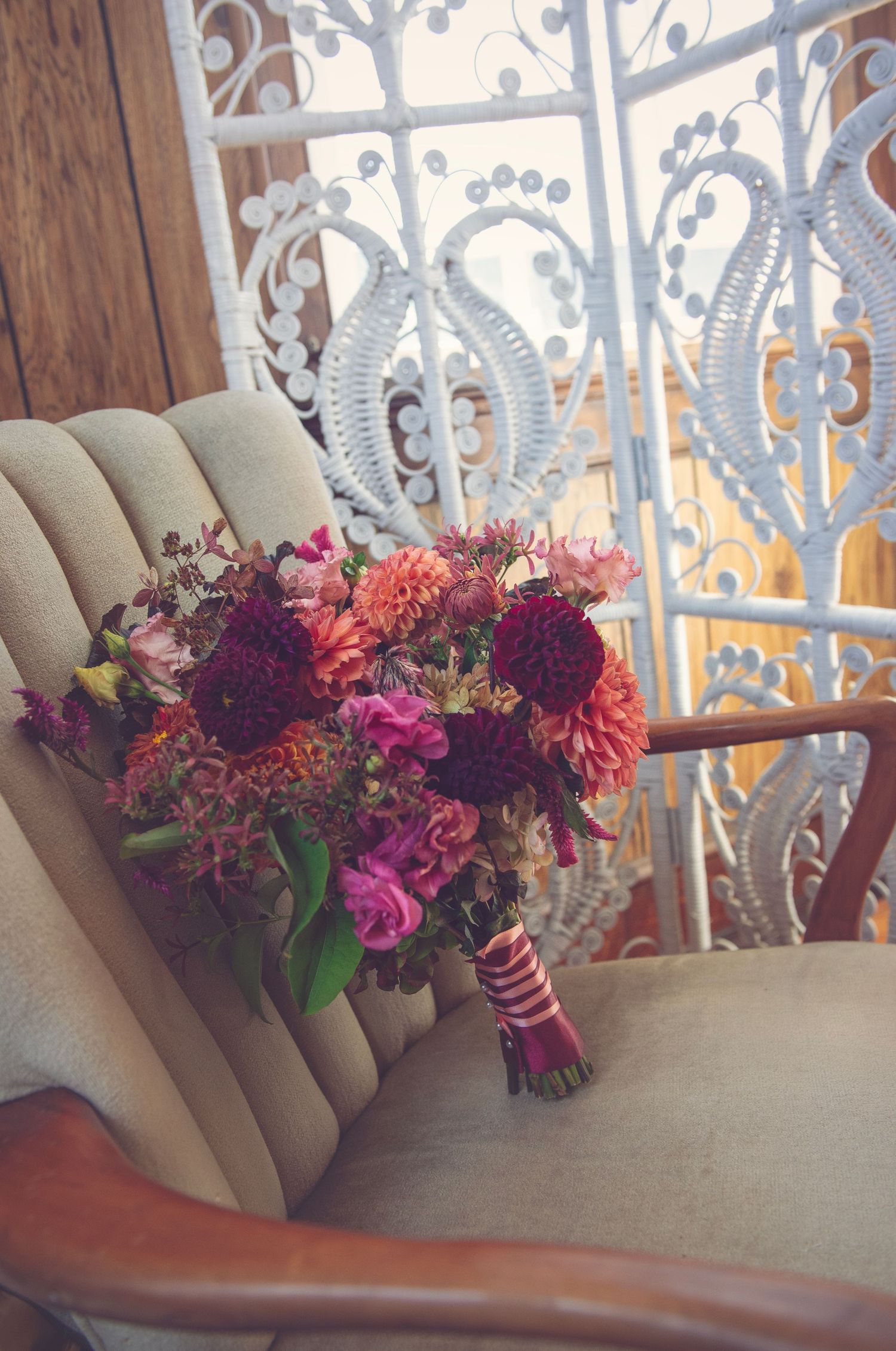 Vibrant floral arrangement with purple and pink blooms on beige couch by ornate window.