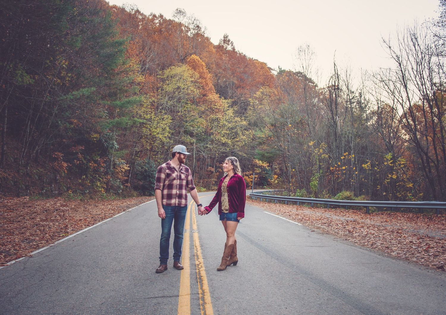 Romantic autumn photoshoot on empty road surrounded by fall foliage.