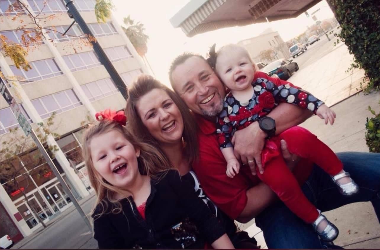 Playful outdoor family portraits with red clothing against brick building.