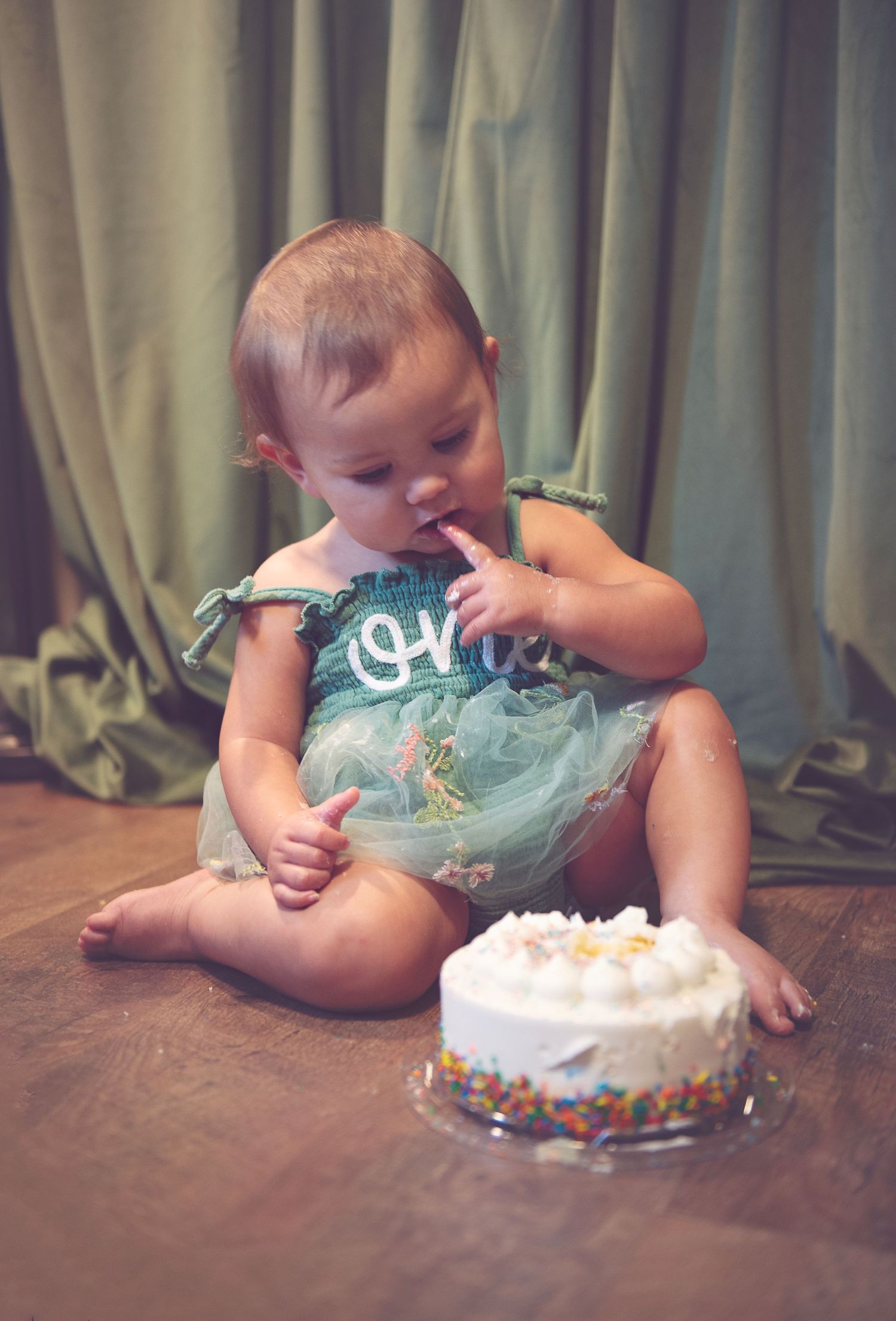 Baby's first birthday cake smash photos with teal outfit and white frosted cake.