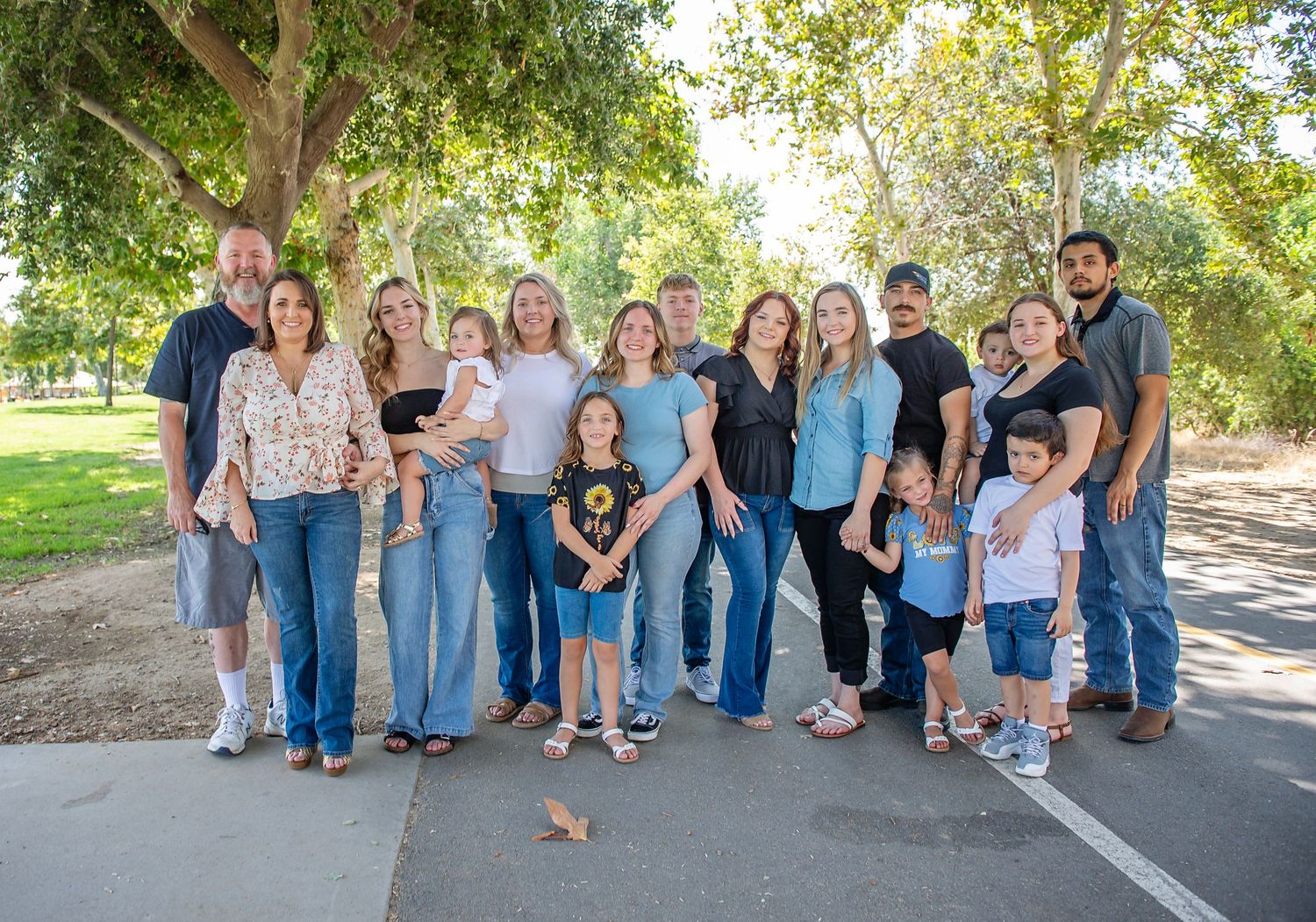 Candid group portrait of friends and family gathered outdoors under green trees.