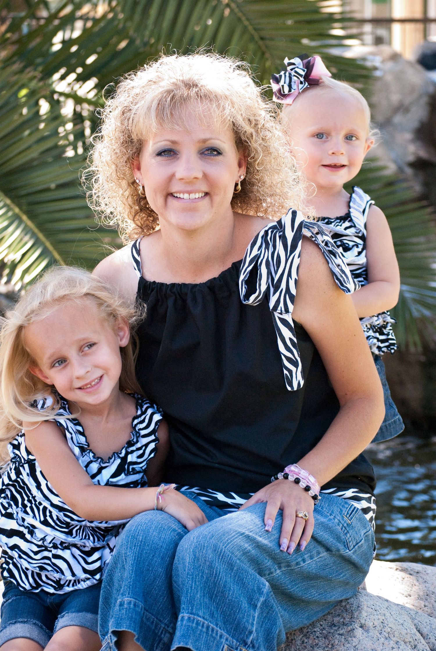 Casual outdoor family portrait with mother and children wearing coordinated black and zebra print outfits.
