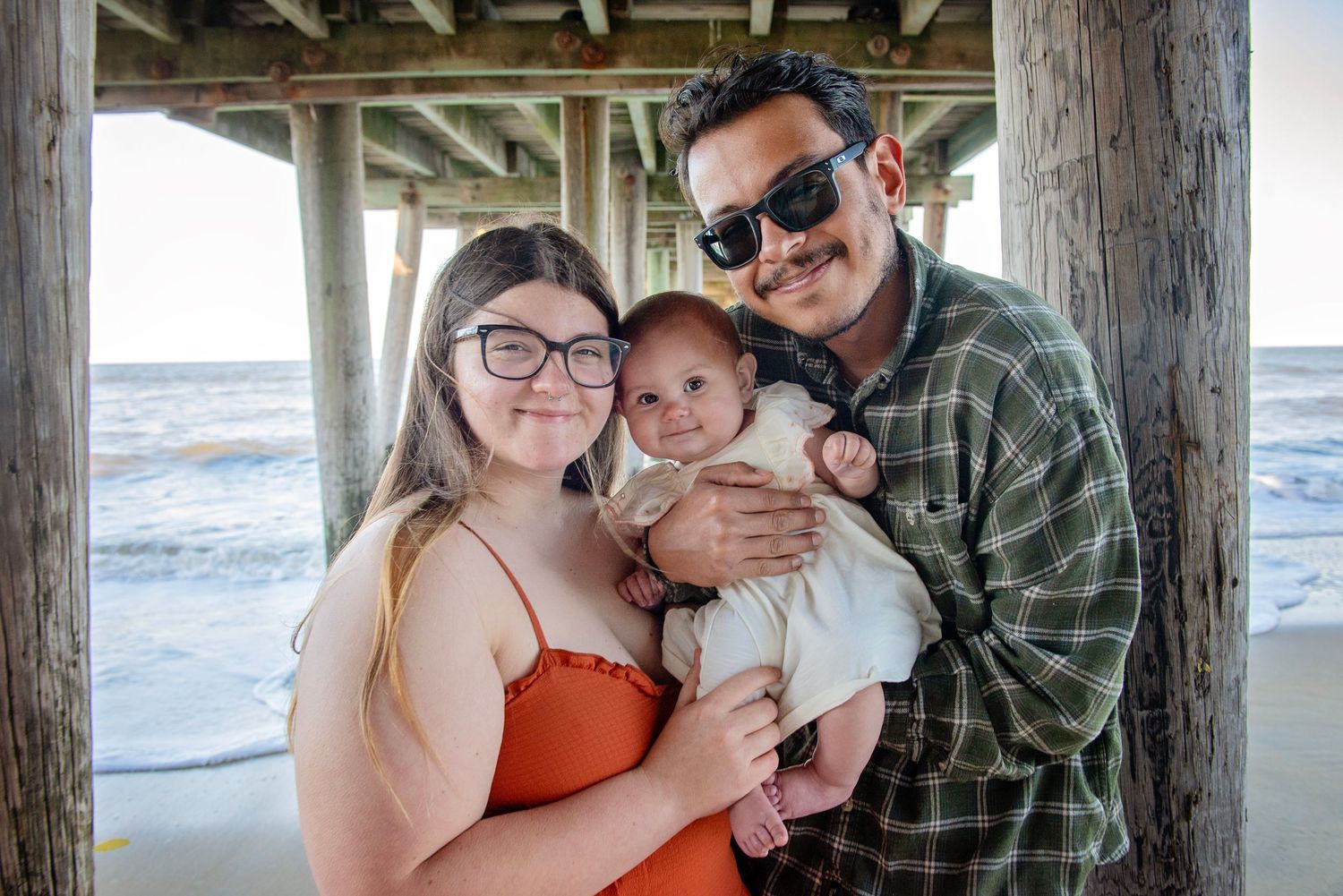 Casual family photos under a wooden pier at the beach during sunset.