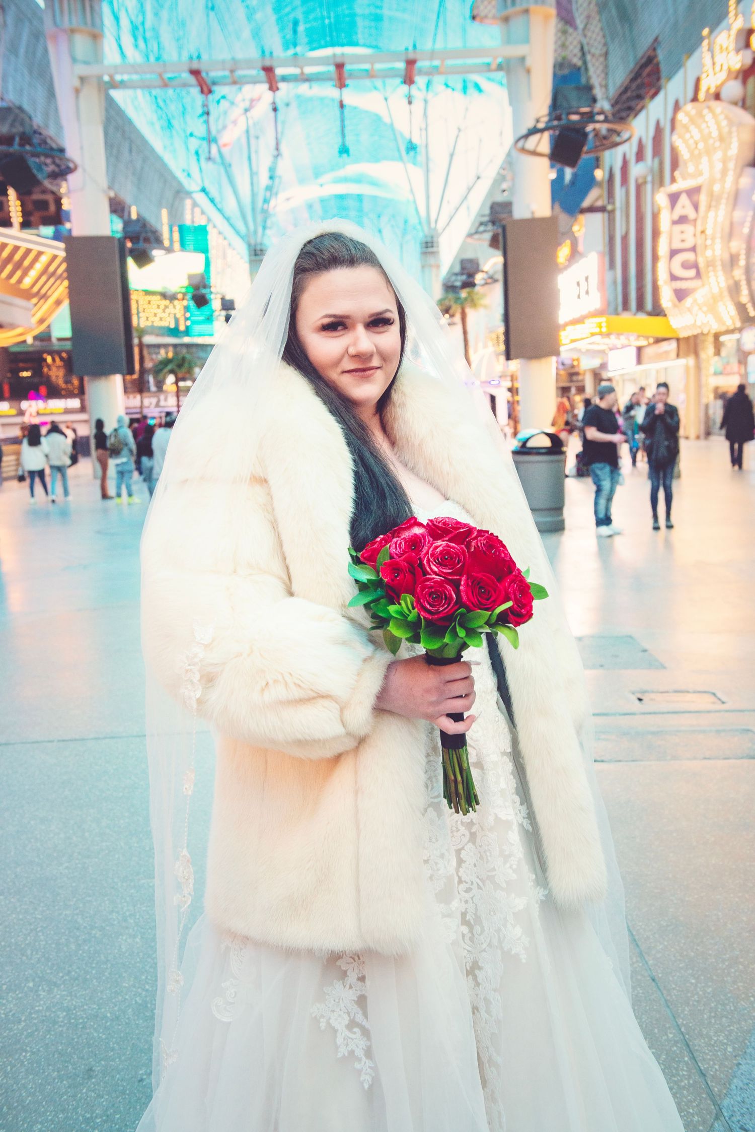 Bride in white fur coat holding red roses in a festive winter setting.