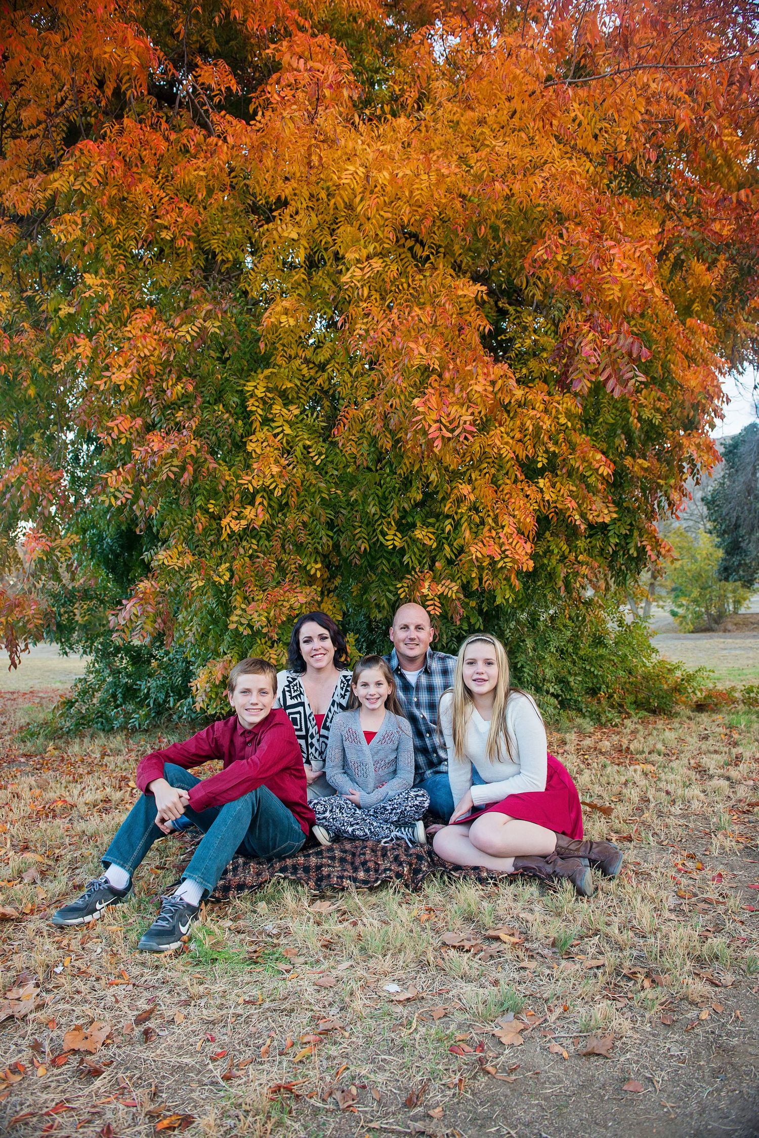 Group relaxing under vibrant orange autumn trees on fallen leaves.