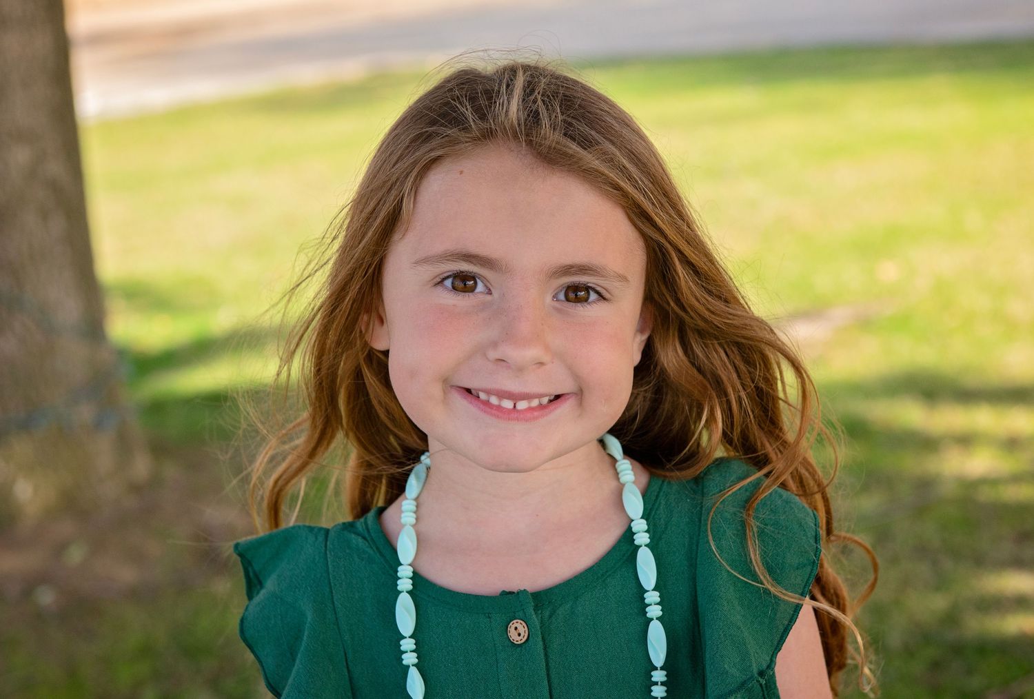 Child in green hoodie smiling outdoors on sunny day.