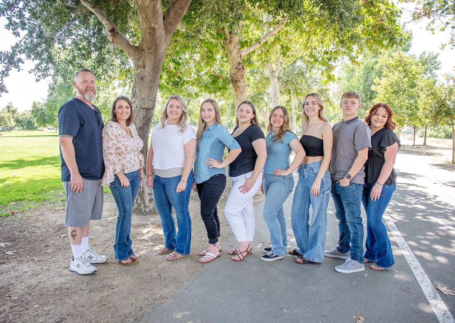 Large group photo of friends sitting casually along a tree-lined pathway.