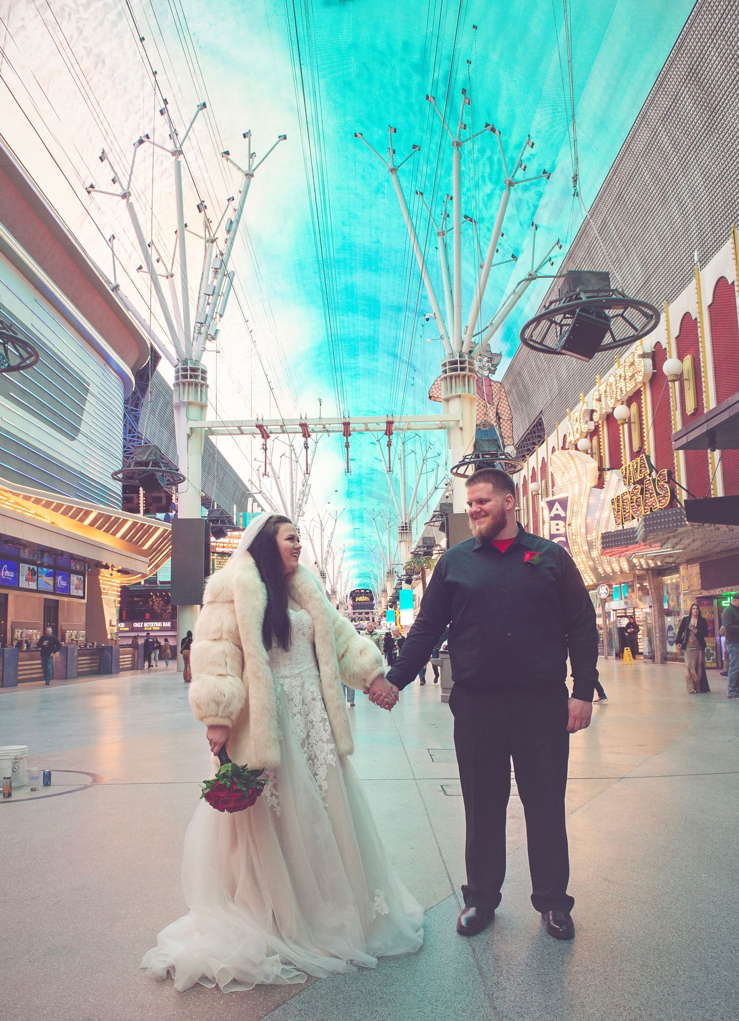 Wedding couple walks under bright turquoise ceiling on Fremont Street in Las Vegas.