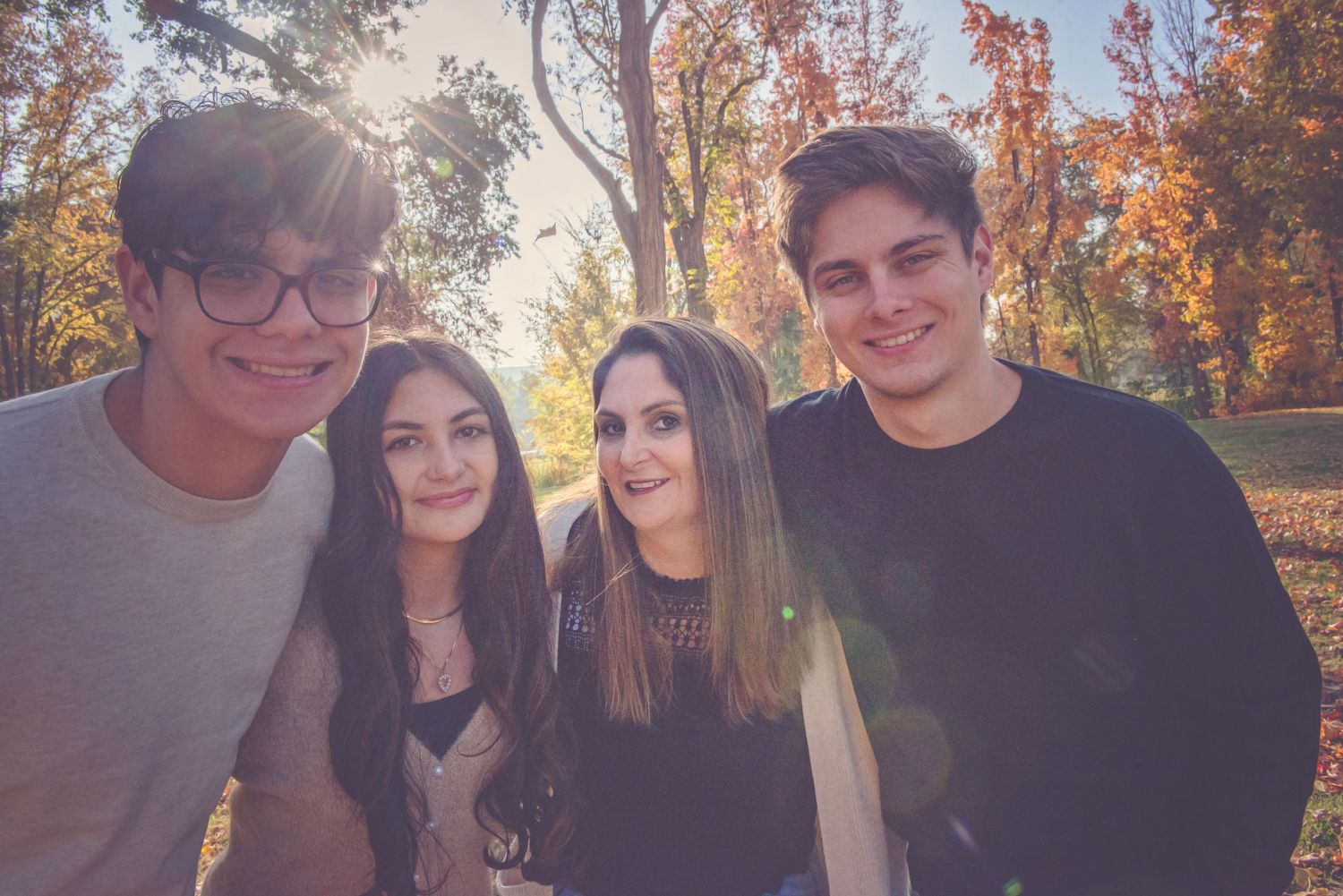 Group of friends gathered outdoors during fall season with trees in background.