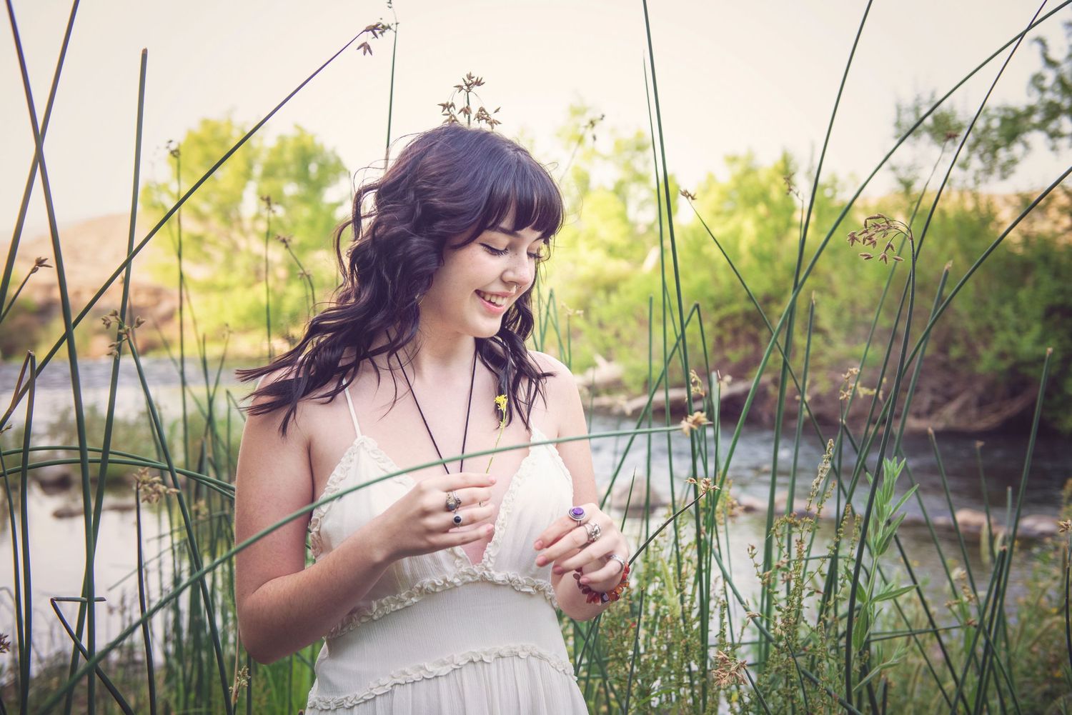 Figure in white dress plays with water while sitting along riverbank.