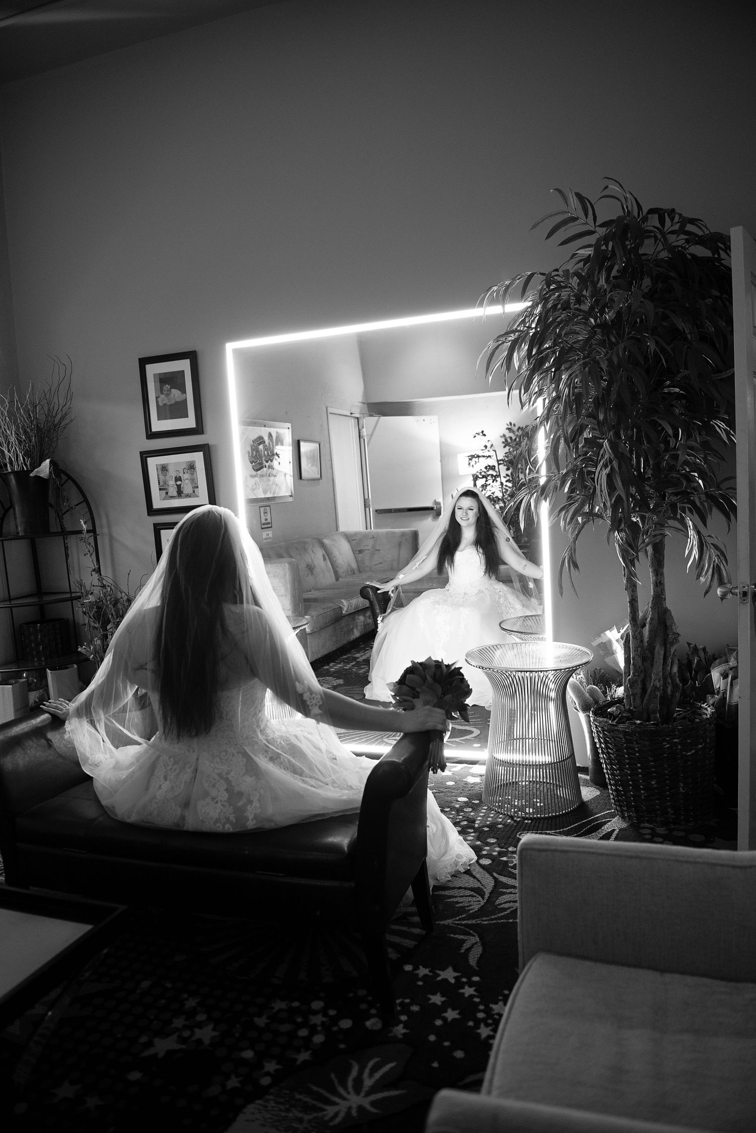 Black and white silhouette of bride in wedding dress getting ready in dimly lit room.