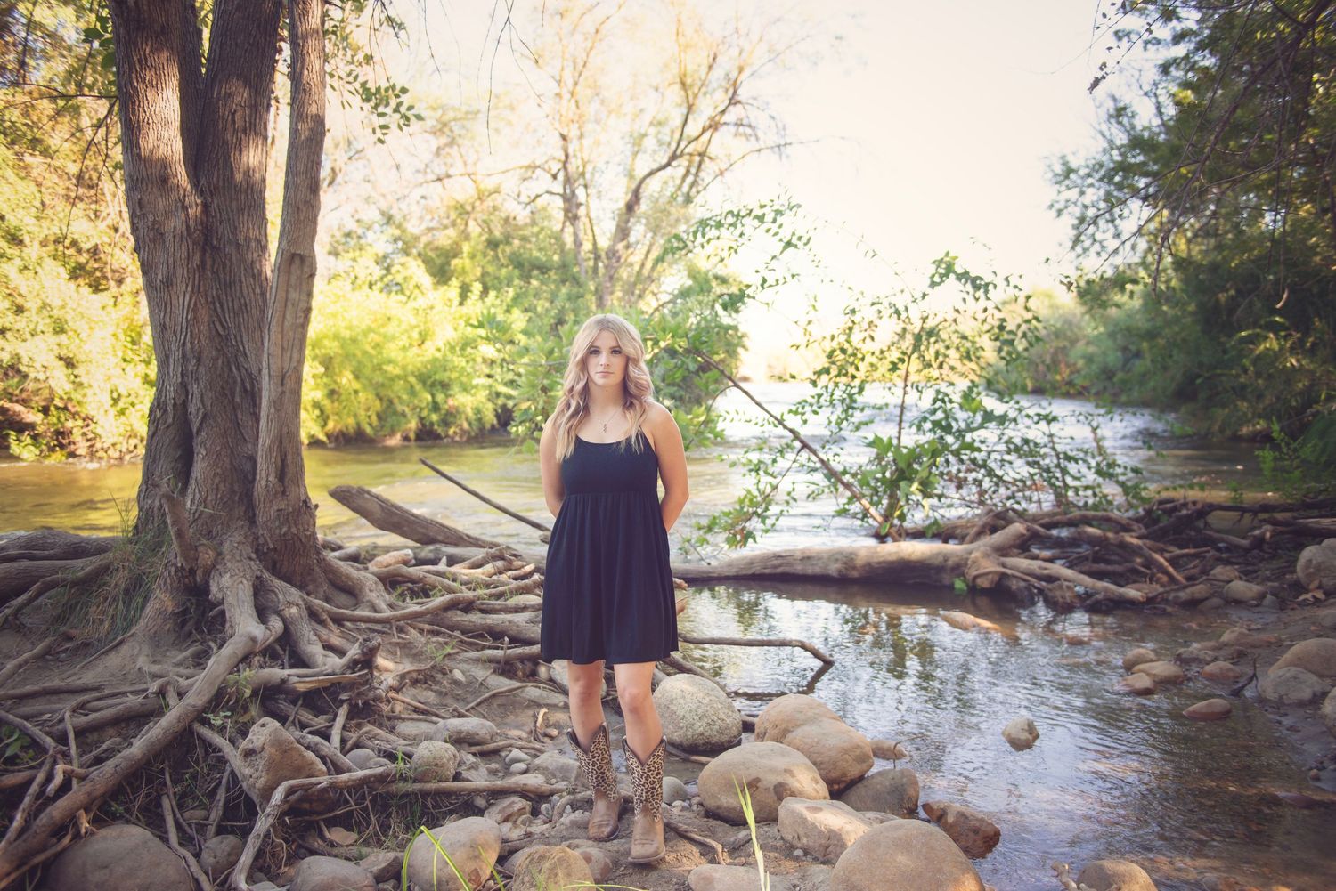 Natural outdoor photoshoot along a riverbank with trees and water in golden sunlight.