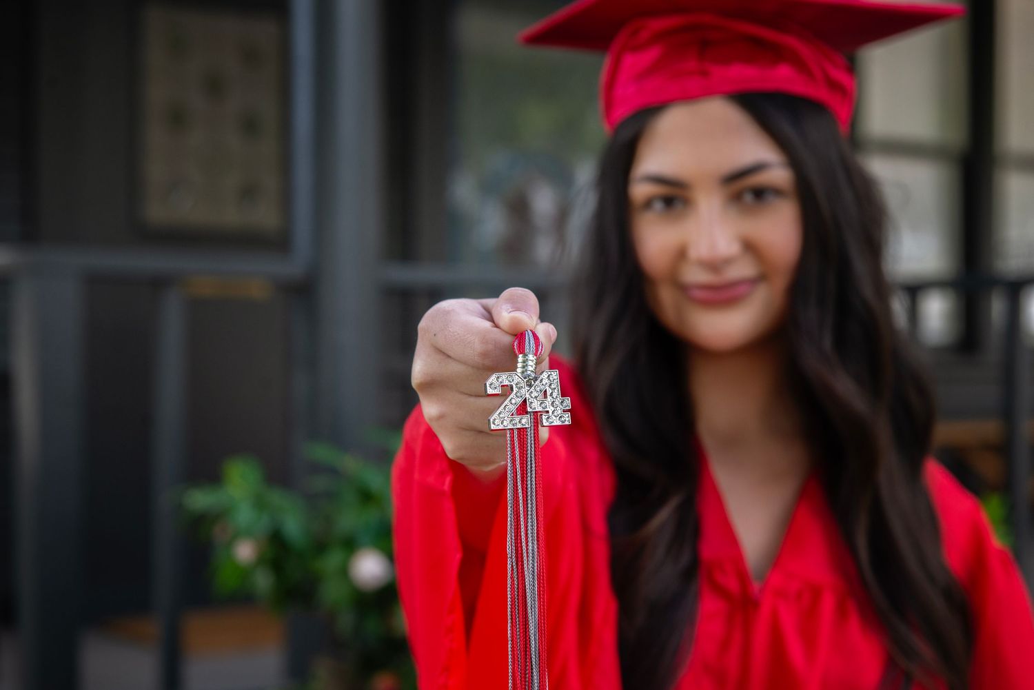 Graduate in red cap and gown holding diploma in front of dark background.