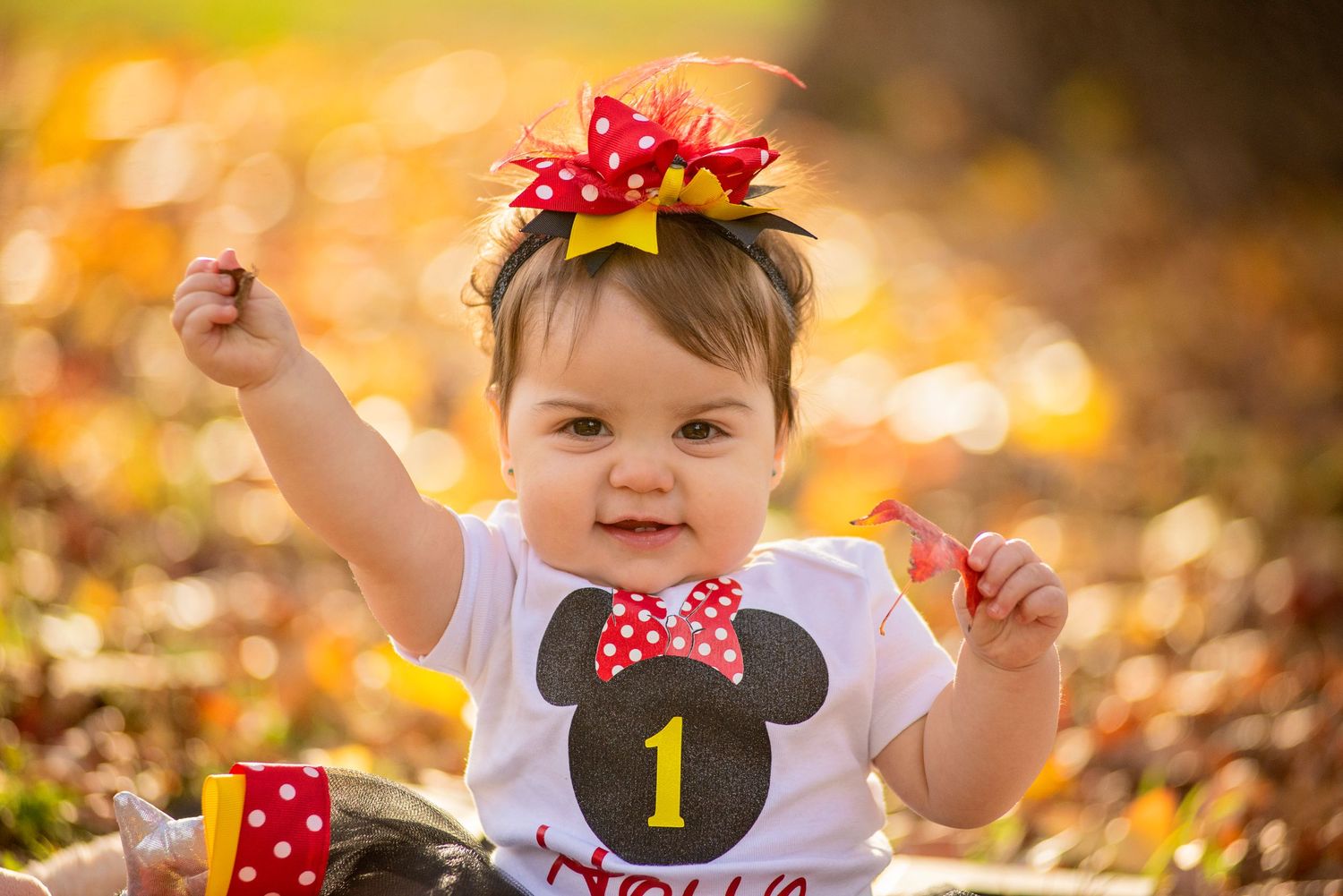 Fall themed first birthday photos with Minnie Mouse inspired outfit and red bow.