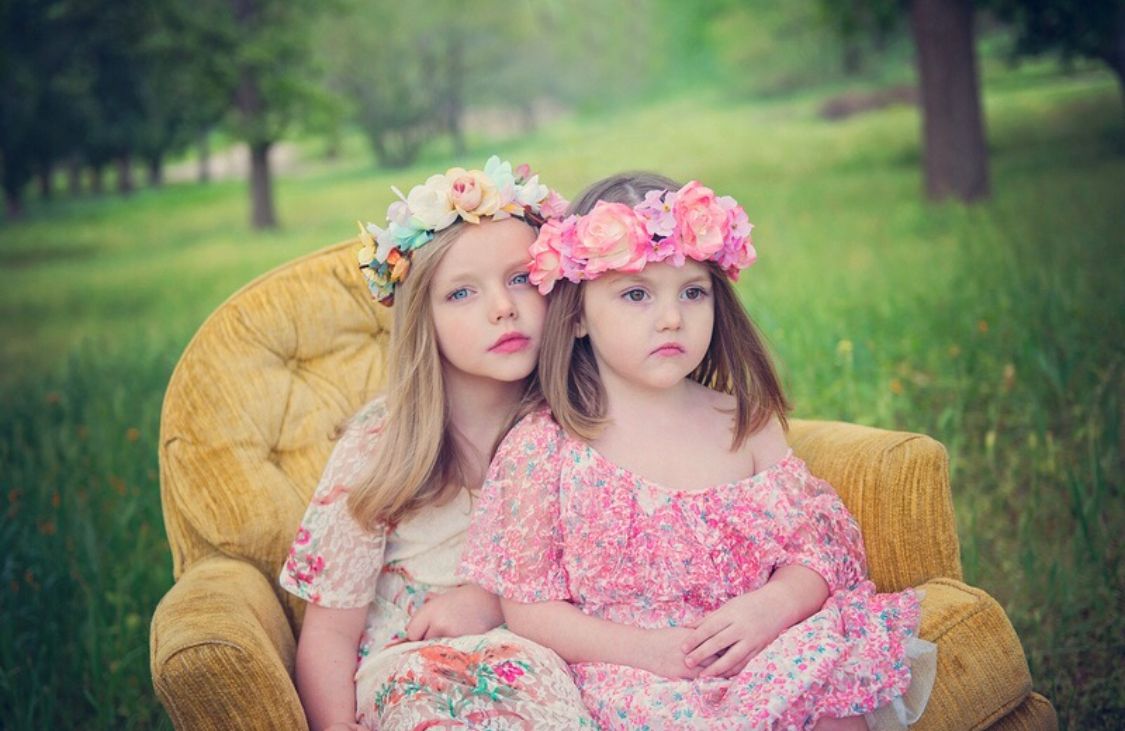 Two figures in floral dresses sit together on a vintage yellow couch in a garden setting.