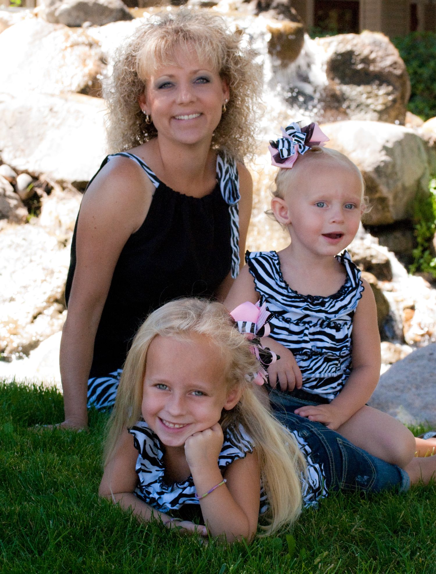 Family portrait of mother and children in matching zebra print outfits sitting on rocks outdoors.