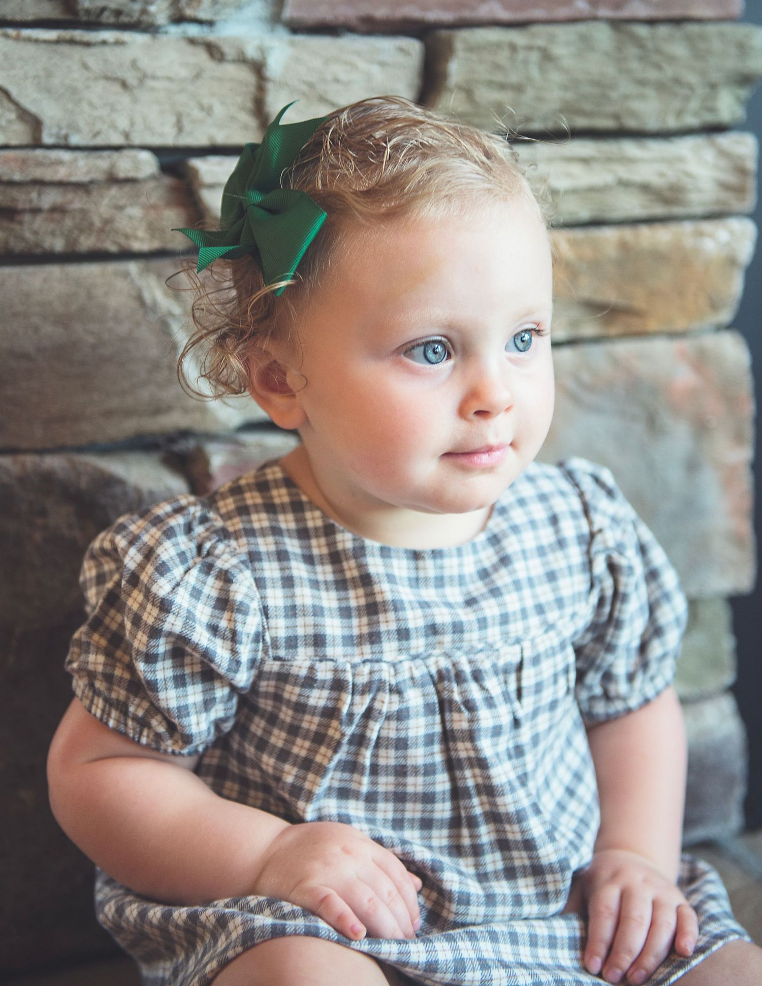 A series of photos showing a baby in a checkered dress sitting against a stone wall background.